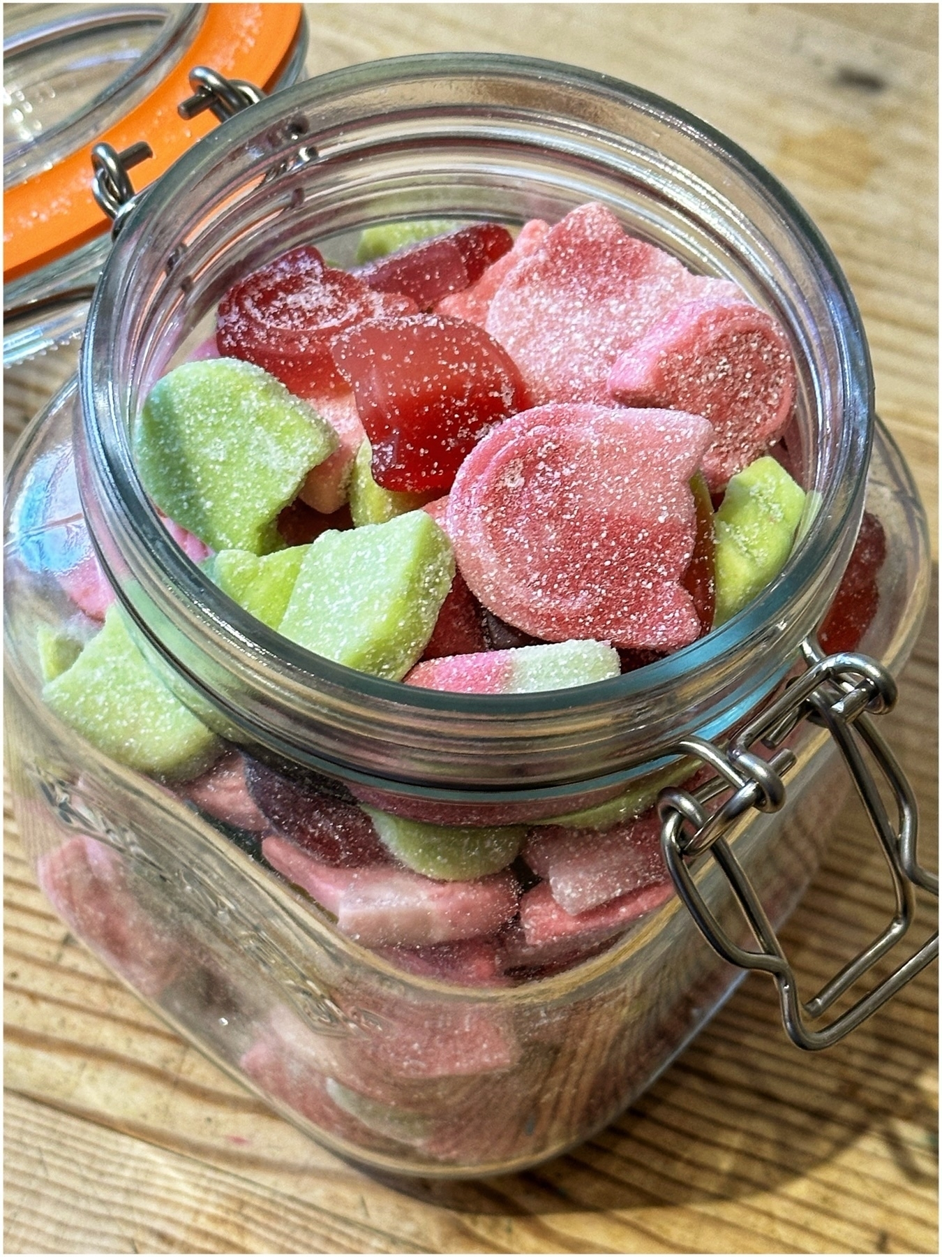 A glass jar filled with various colorful sugar-coated gummy candies on a wooden surface.