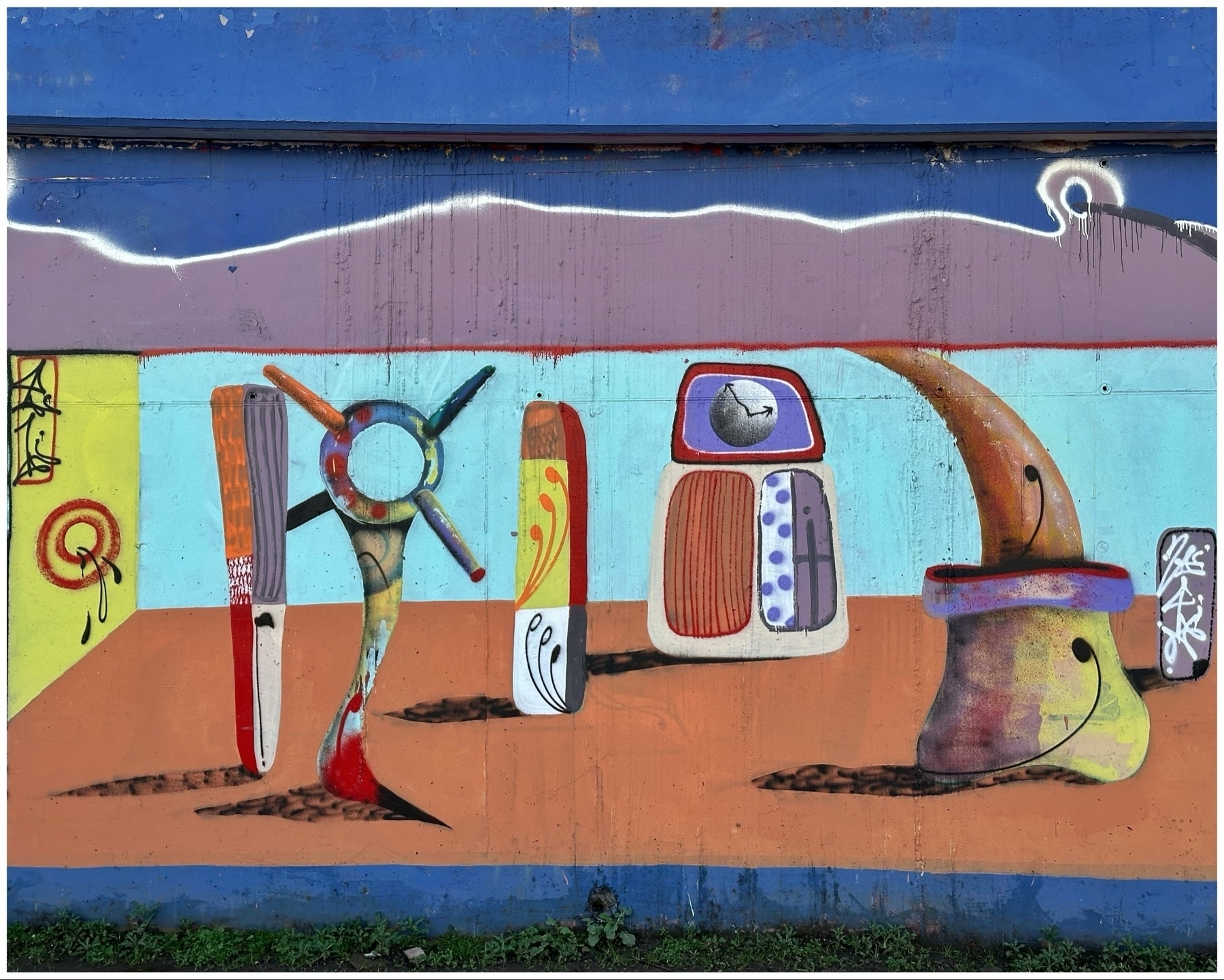 A colorful graffiti mural featuring abstract shapes and forms resembling whimsical figures and objects on an urban wall.
