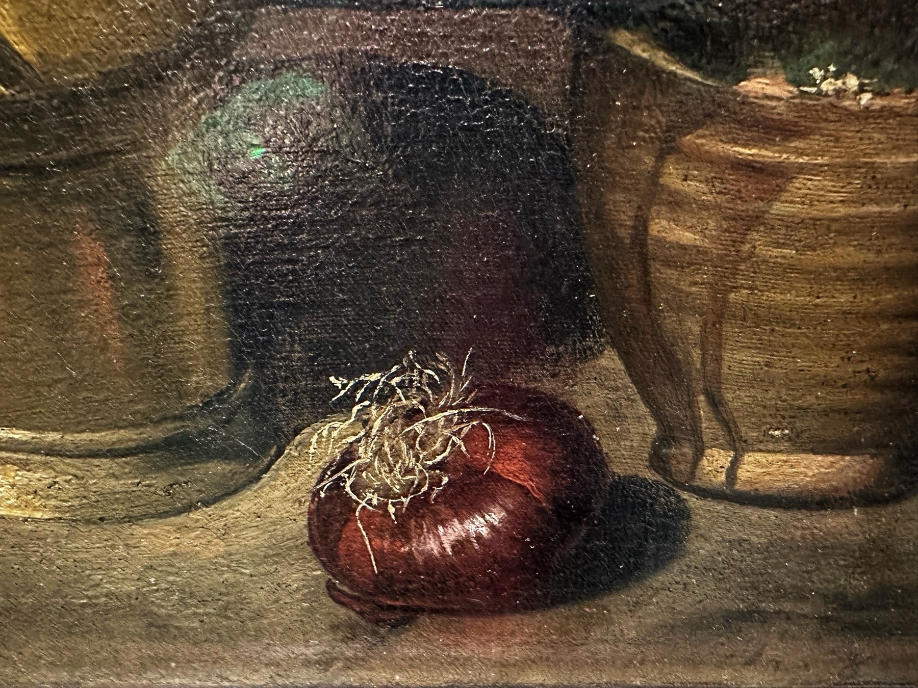 Oil painting close-up of a red onion with roots on a wooden surface, against a dark background with partially visible earthenware vessels.