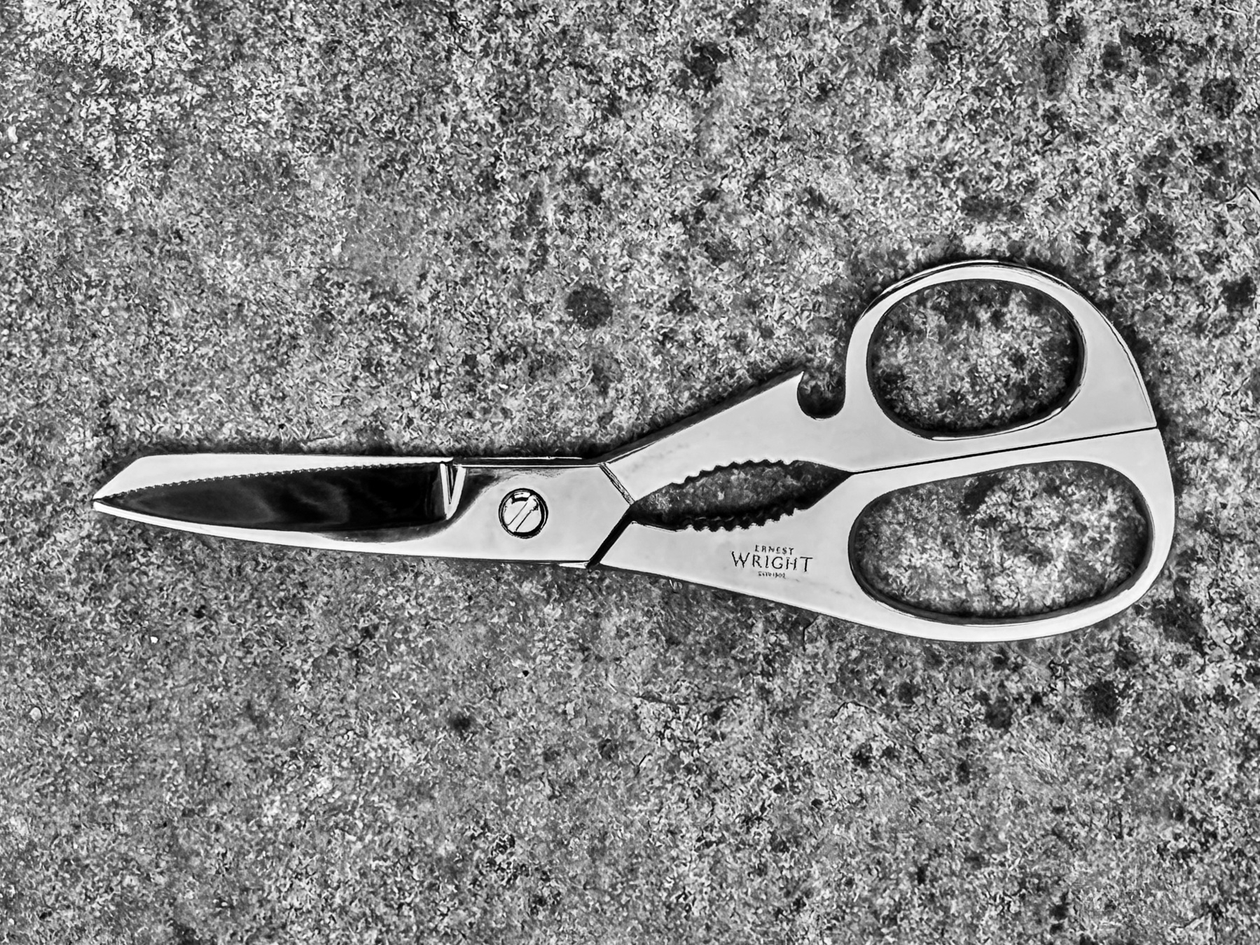 A high contrast black and white photograph of scissors on a stone surface. 