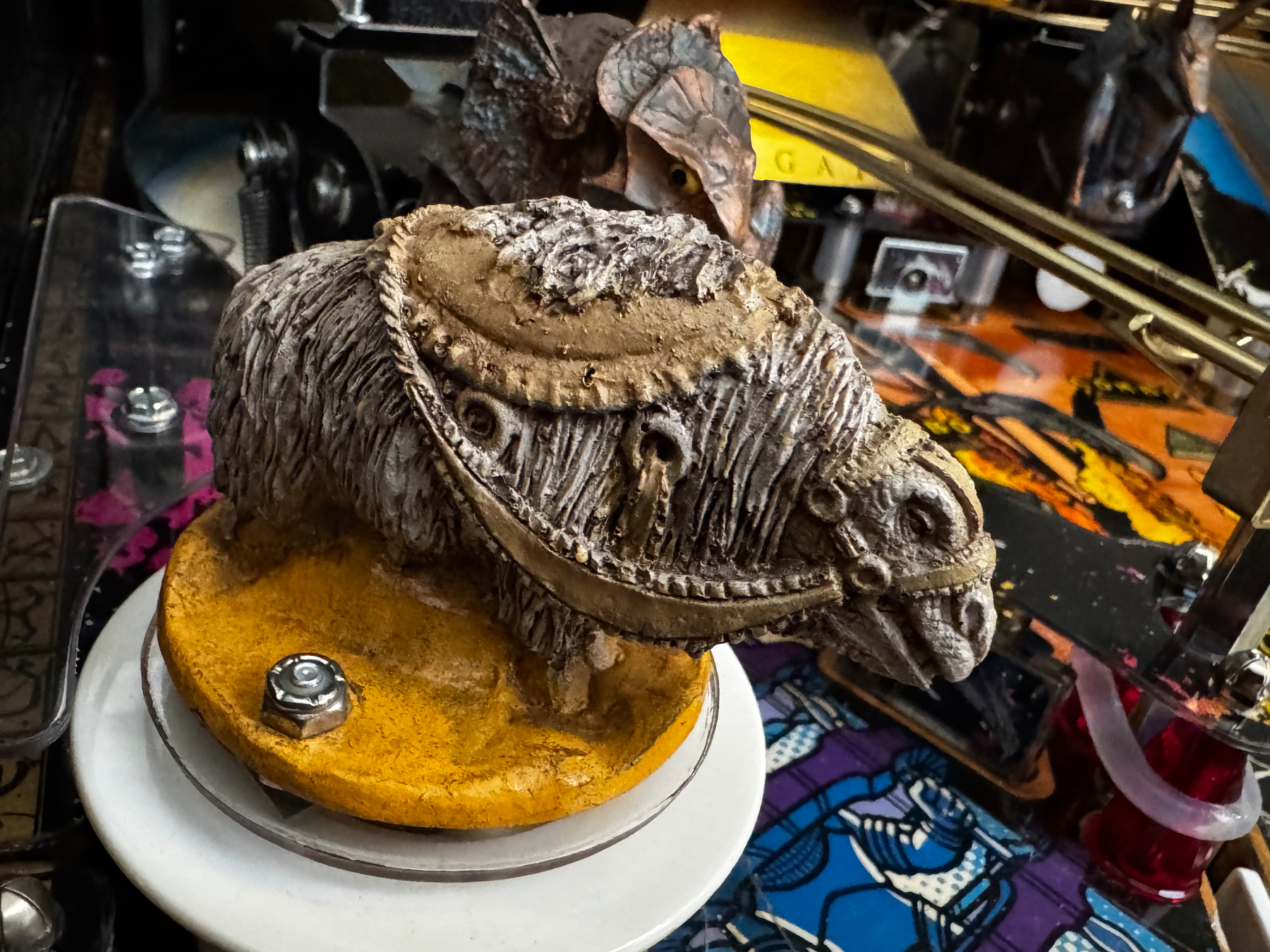 A detailed miniature figure of a shaggy creature with a harness is mounted on a spinning platform amidst a colorful, mechanical environment.