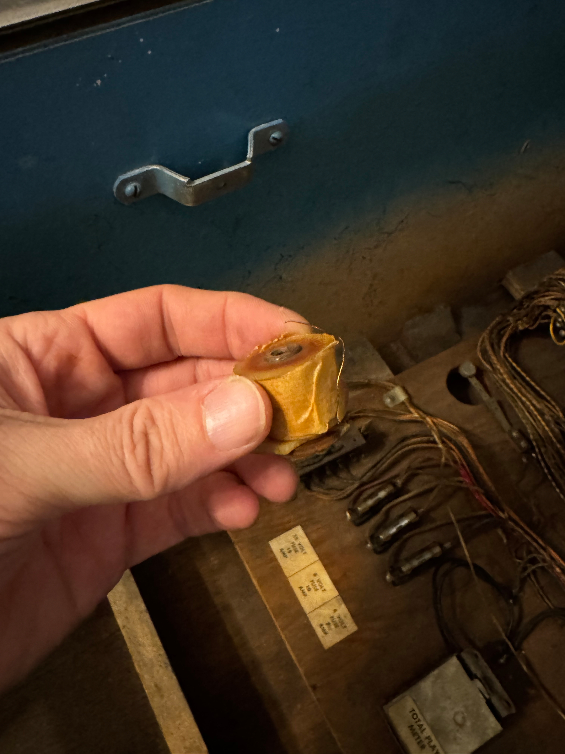 A hand is holding a vintage relay coil component with wires in an old pinball cabinet.