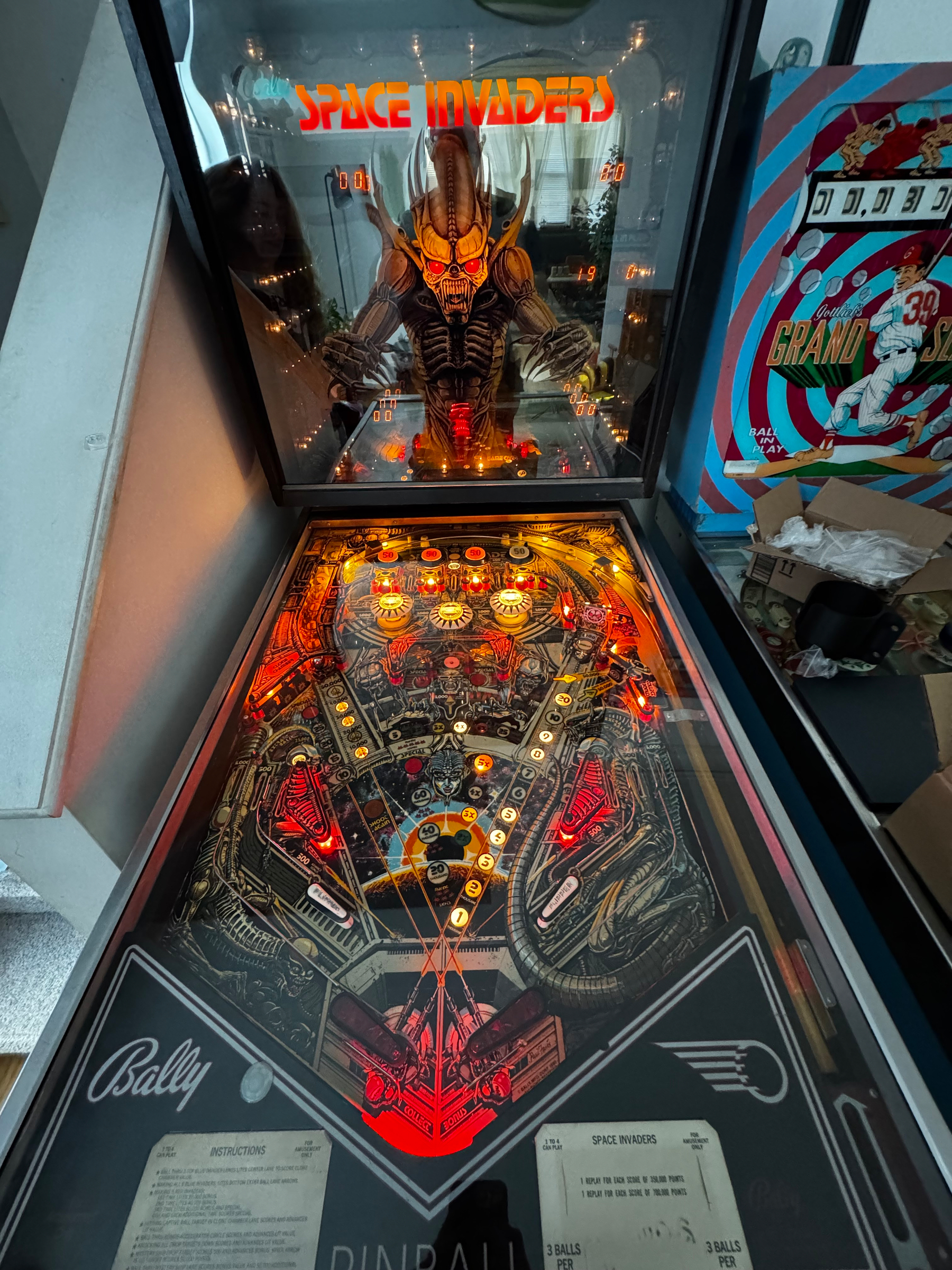 A vintage Space Invaders pinball machine features an illuminated, colorful playfield with sci-fi themed artwork.