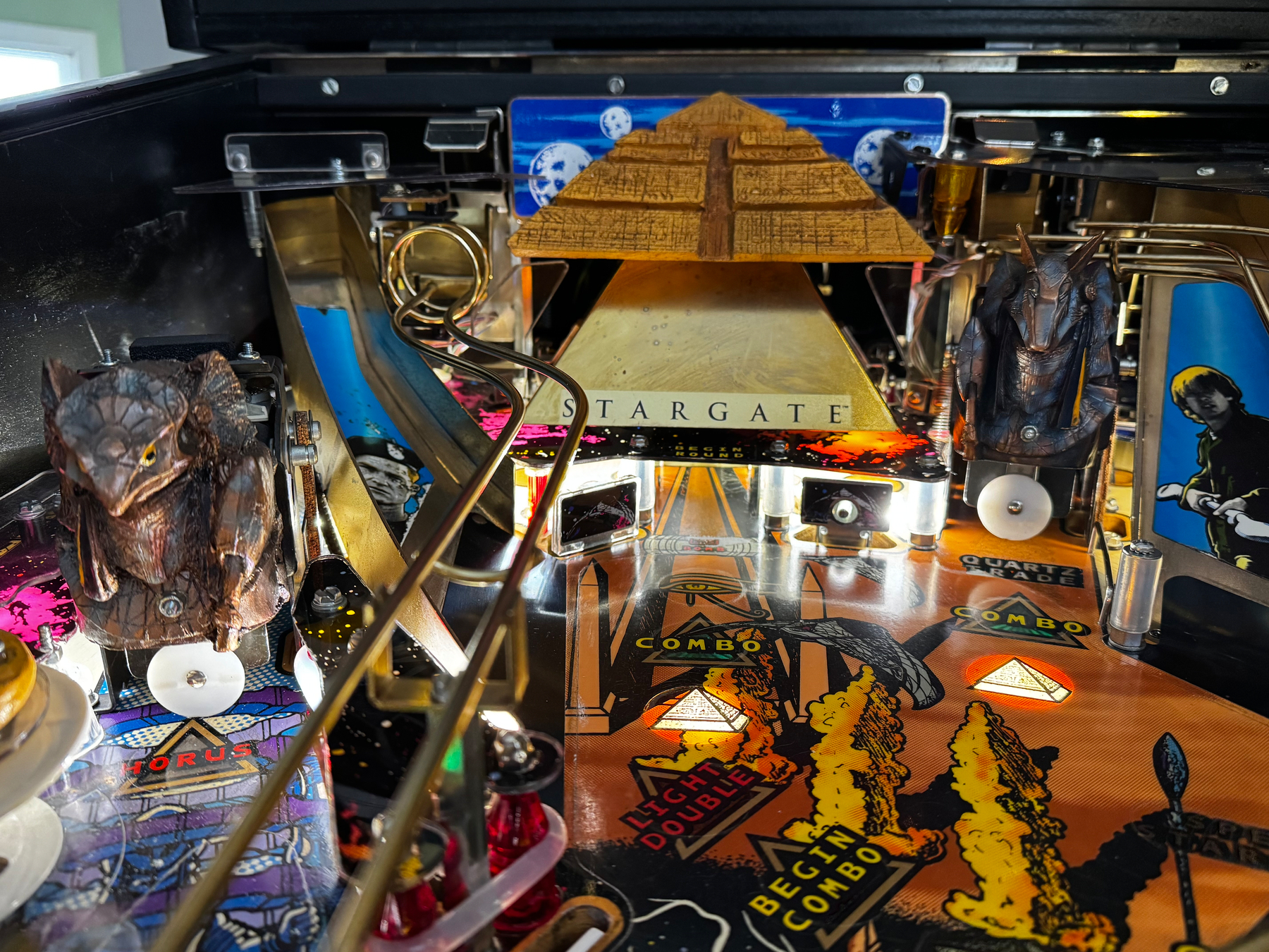 A detailed view of a Stargate themed pinball machine, featuring elements like a pyramid, ramps, and decorative figures.