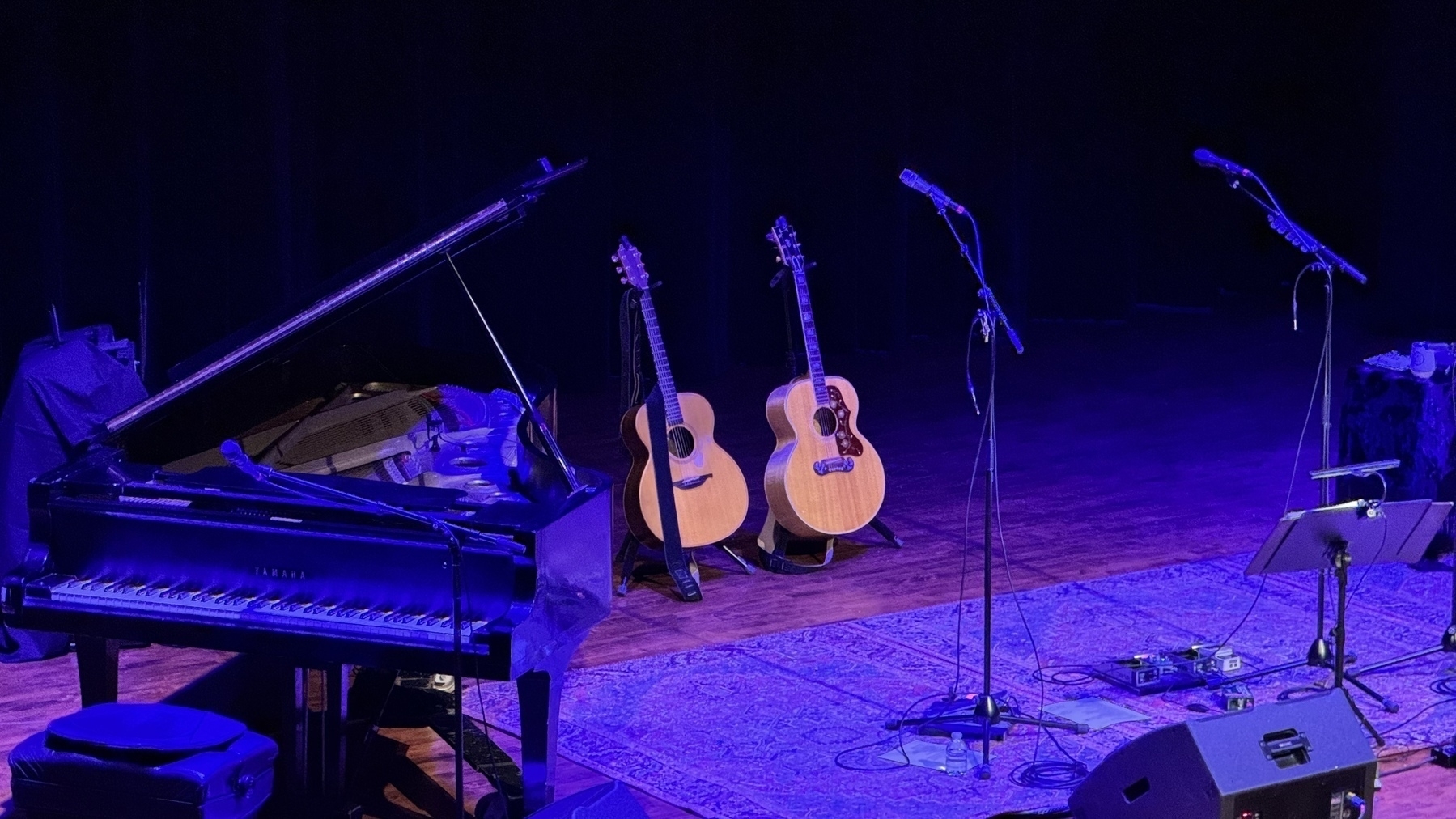 An empty stage with a grand piano and two guitars. 