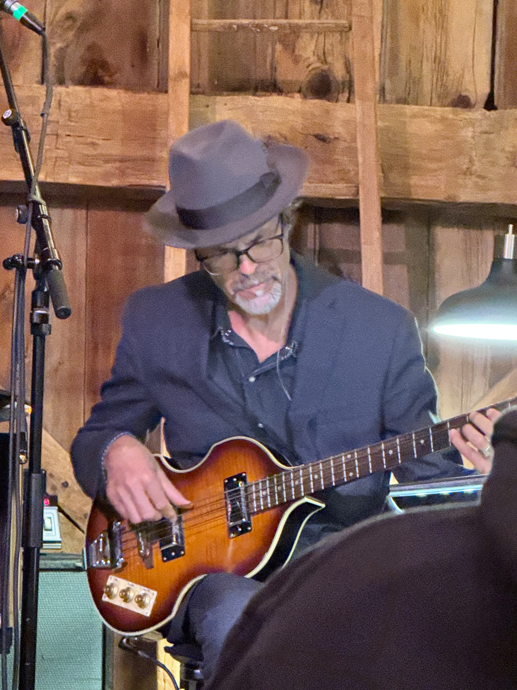 Linford Detweiler is playing an electric bass  in a rustic in the barn at Nowhere Else Farm