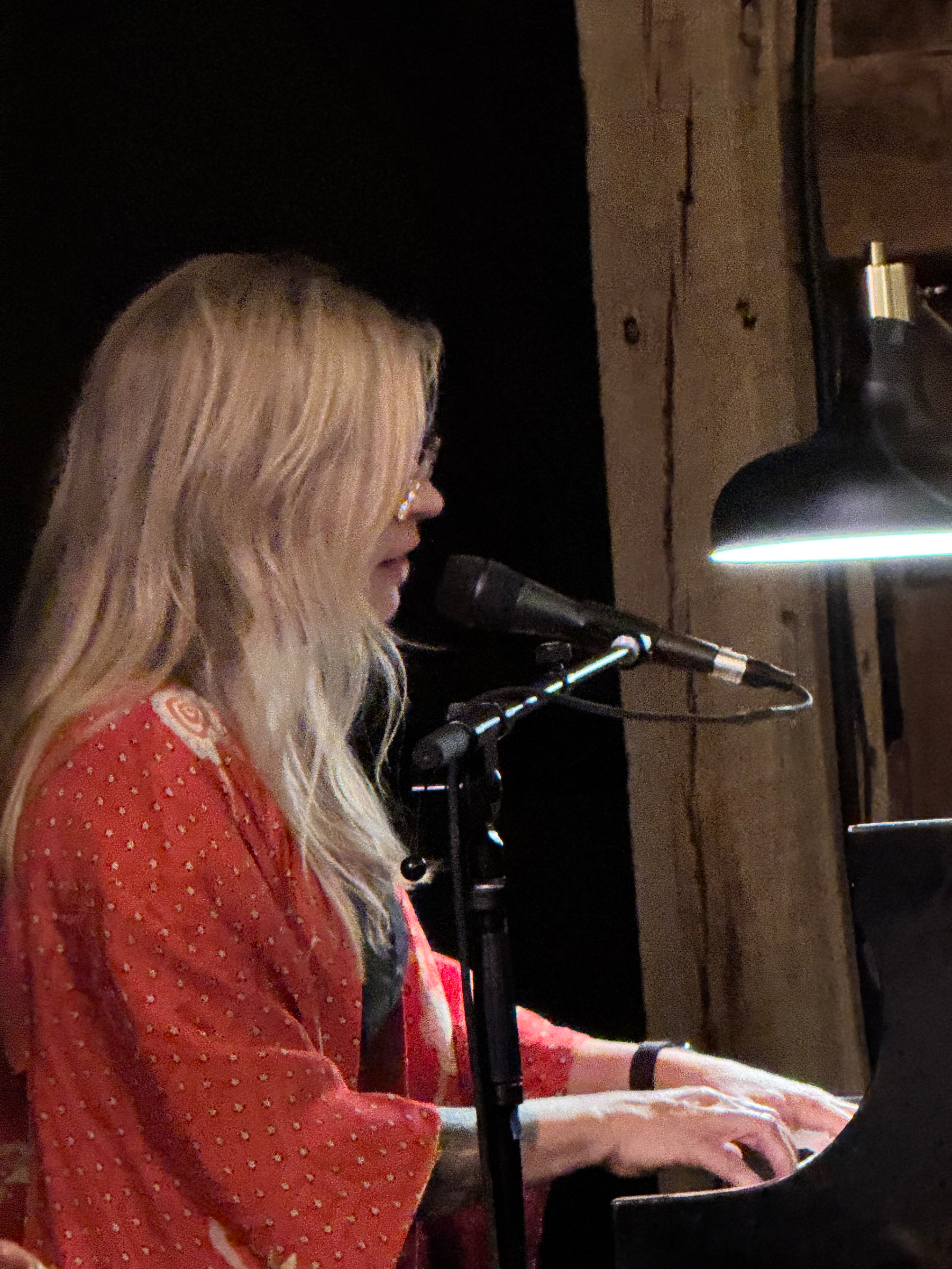 Karin Bergquist playing the piano and singing into a microphone under soft lighting in the barn at Nowhere Else Farm.