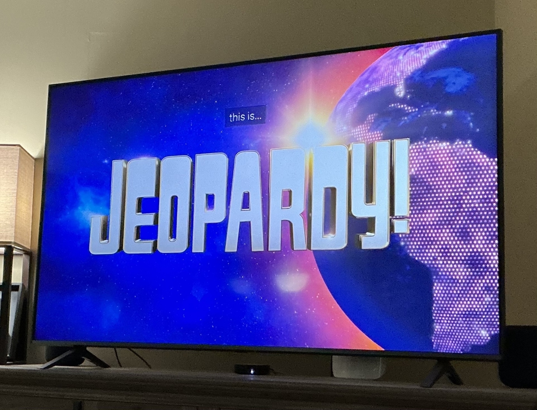 A television screen displays the title Jeopardy! with a background of the Earth and space.