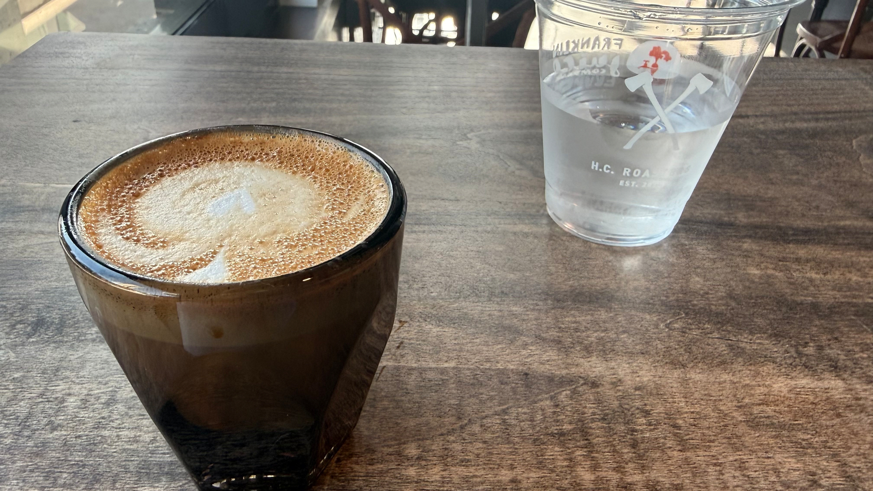 A cortado and a glass of water are placed on a wooden table.