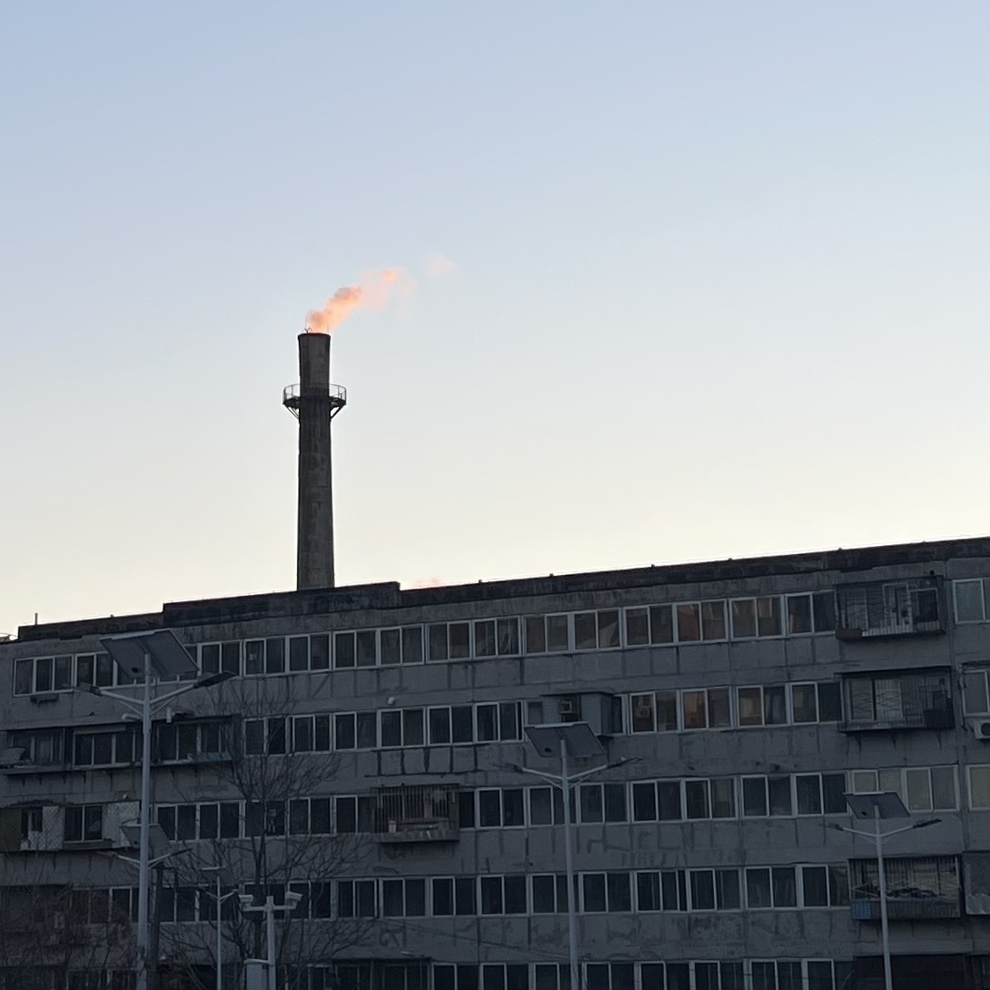 The smoke rising from the chimneys on the way to school these past few days has been glowing orange under the morning sun. (A factory building with a tall chimney emits orange smoke against a clear sky.)