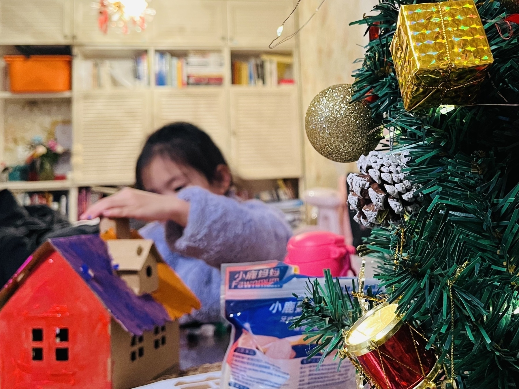 Hamer assembled her cardboard house and carefully colored it. (A child is assembling a gingerbread house near a decorated Christmas tree.)