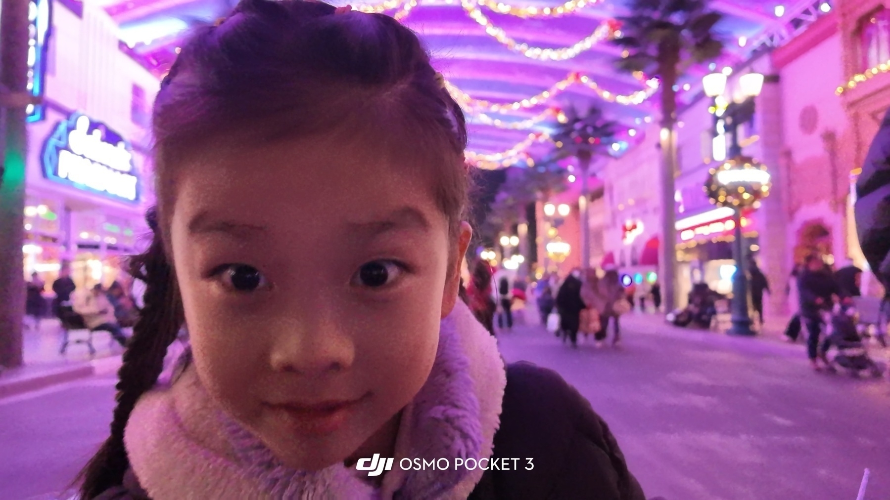 Hamer stared at the camera in such a funny way. (A young girl poses for a photo in a brightly lit, festive indoor street setting.)