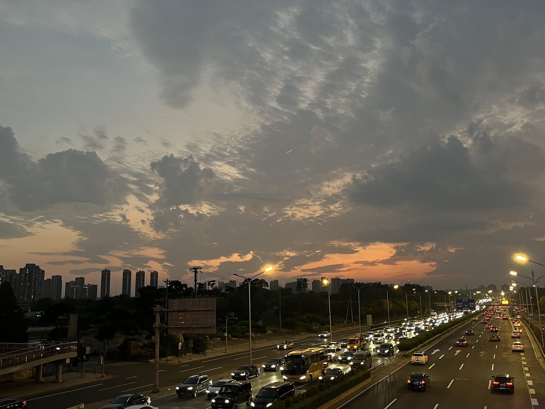 A bustling highway is seen at dusk, with city buildings silhouetted against a colorful, cloud-filled sky. I caught a glimpse of fiery clouds on my way home.