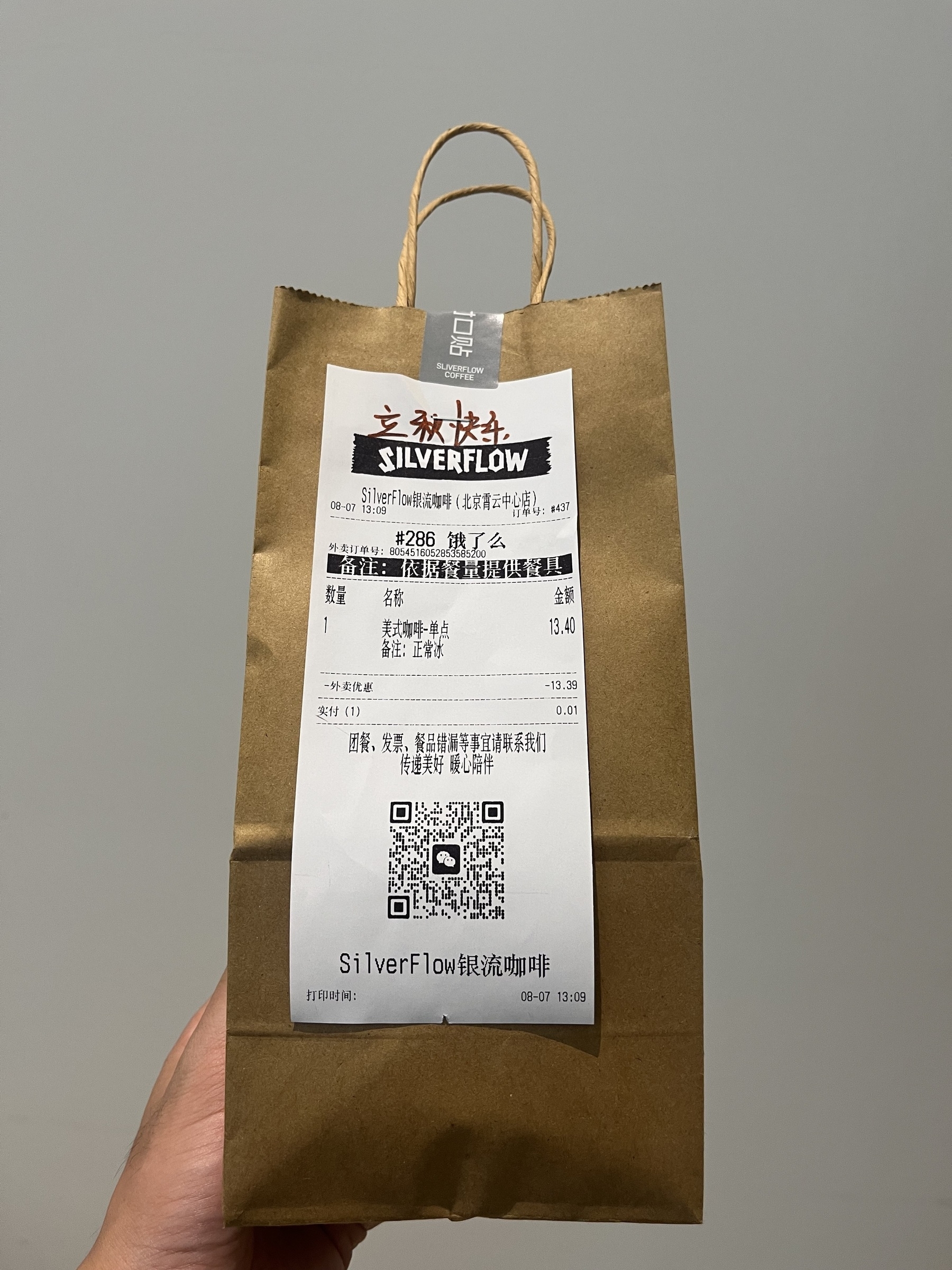 A hand holds a brown paper bag with a Silverflow coffee, for Start of Autumn.
