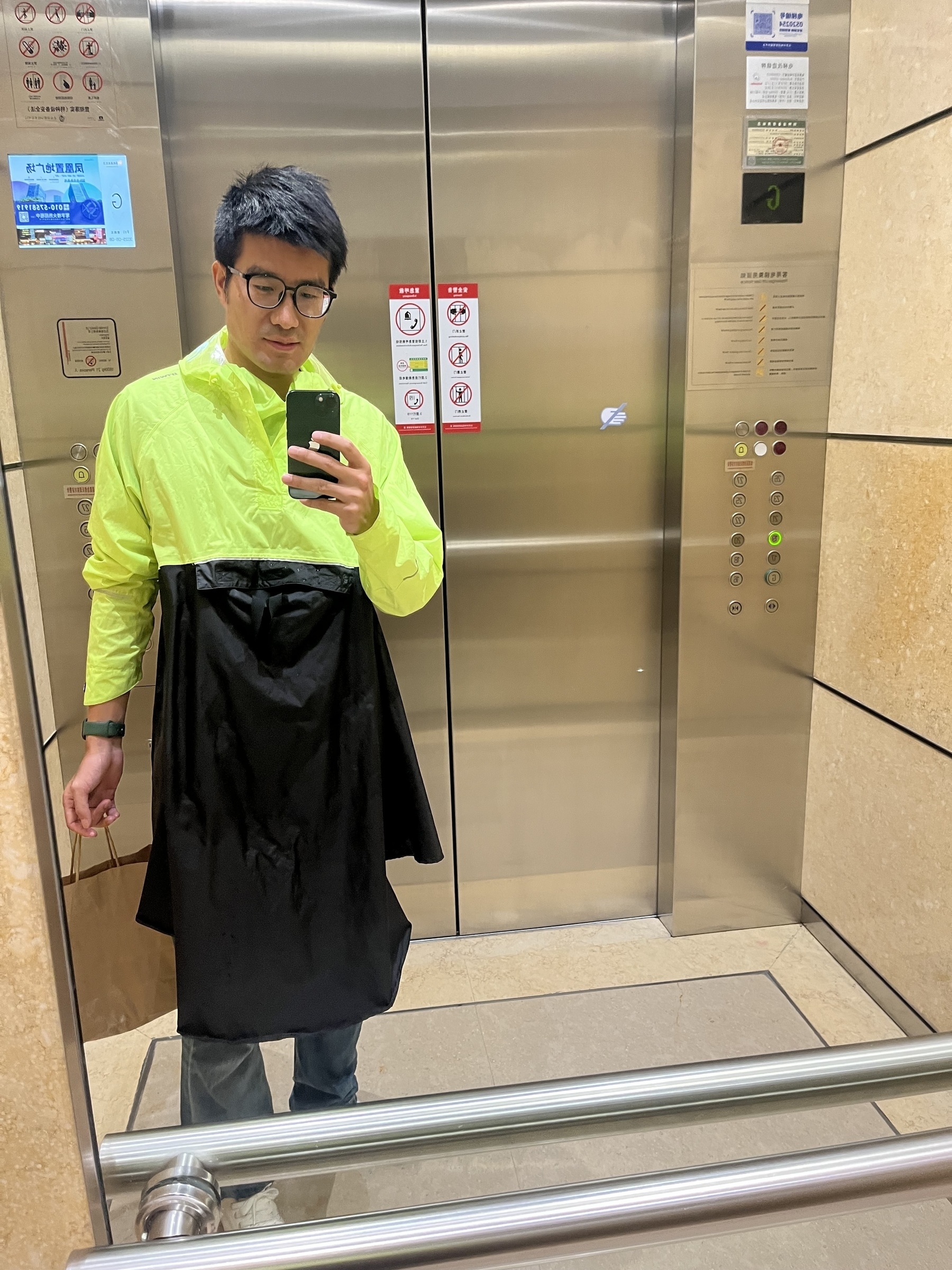 A person wearing a neon yellow and black outfit is taking a mirror selfie in an elevator.
