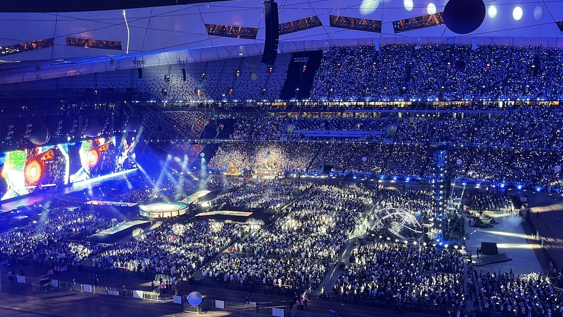 A large crowd is attending a vibrant, illuminated concert or event in a stadium. Mayday’s 5525 concert