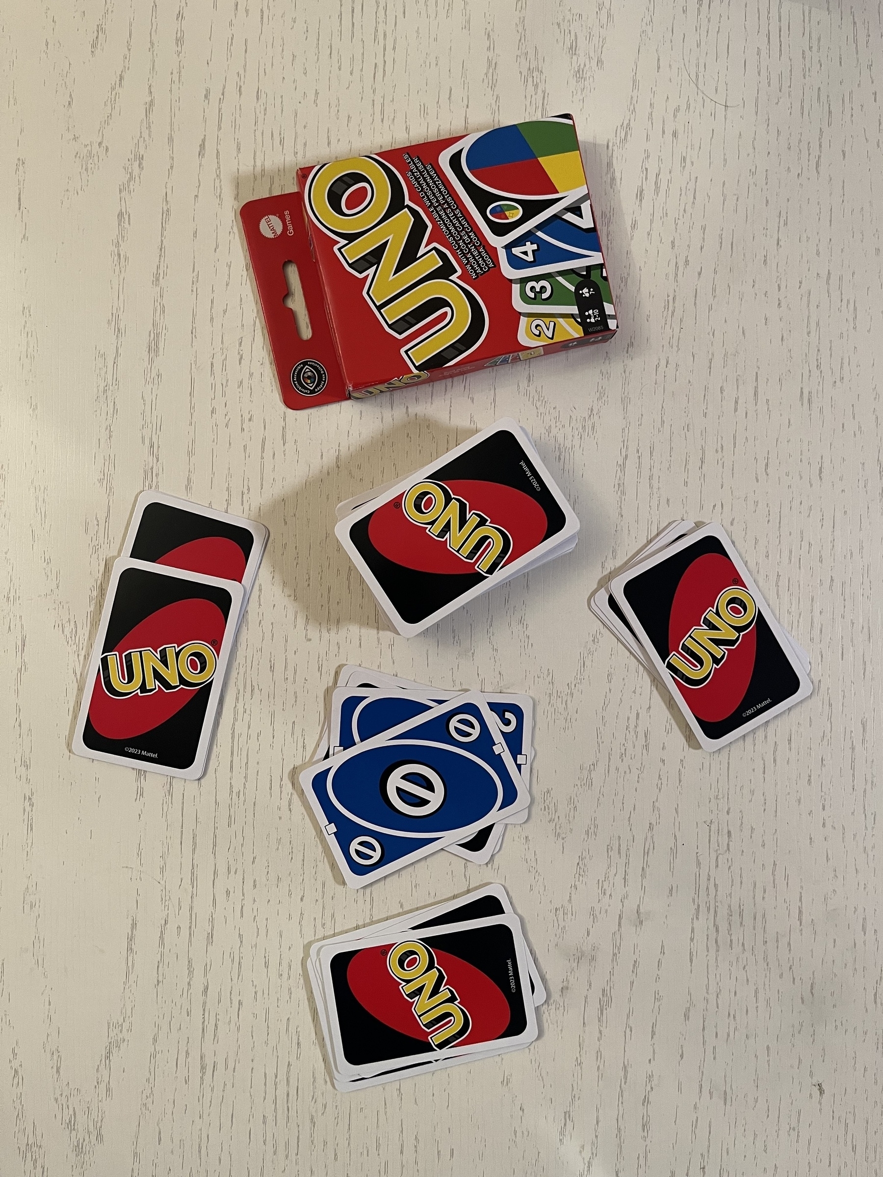 A deck of UNO cards with a few blue cards and others face down on a white surface beside the packaging.