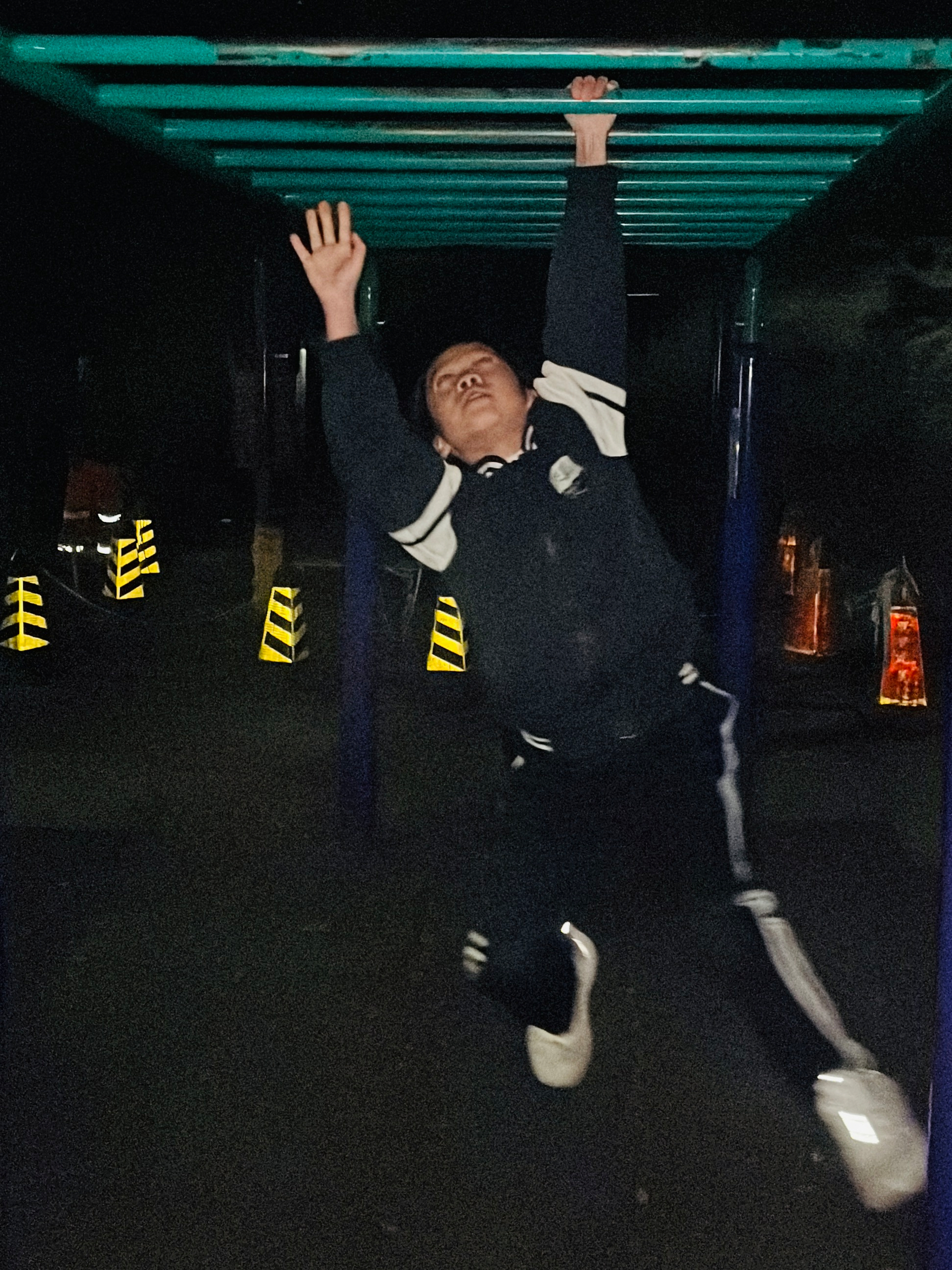 A person is swinging on monkey bars at night, reaching for the next bar.