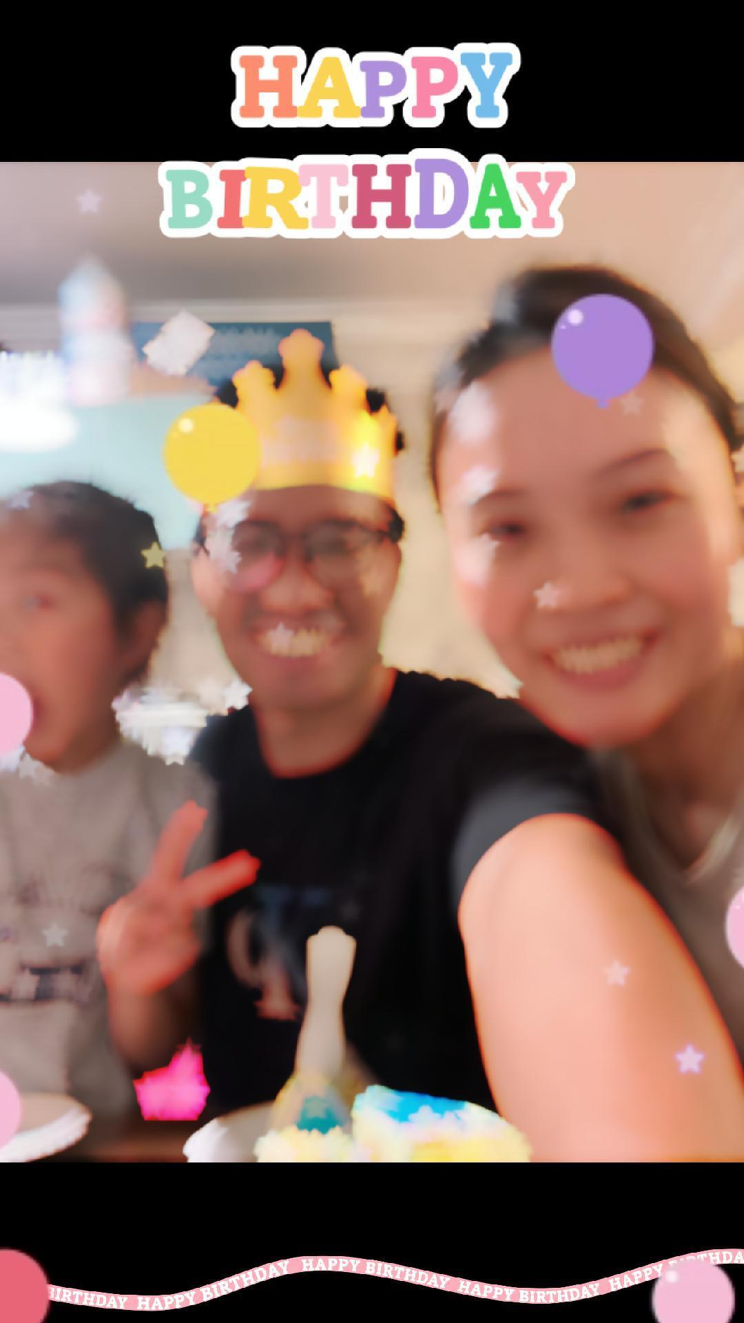 Three people are celebrating a birthday, with one wearing a digital crown filter, surrounded by colorful decorations and balloons.