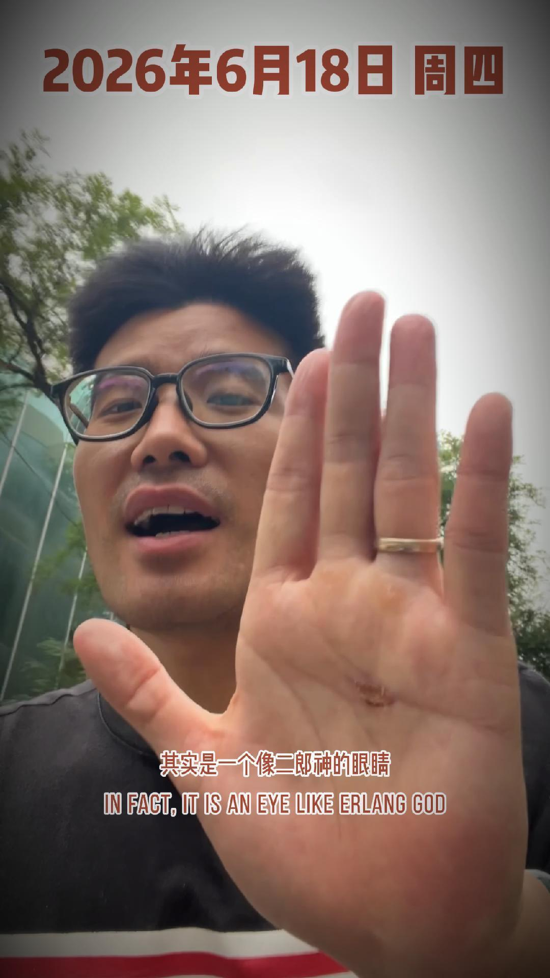 A man wearing glasses is holding up his hand toward the camera with a small mark on his palm, while text indicates the date June 18, 2026, and mentions an eye like Erlang God.