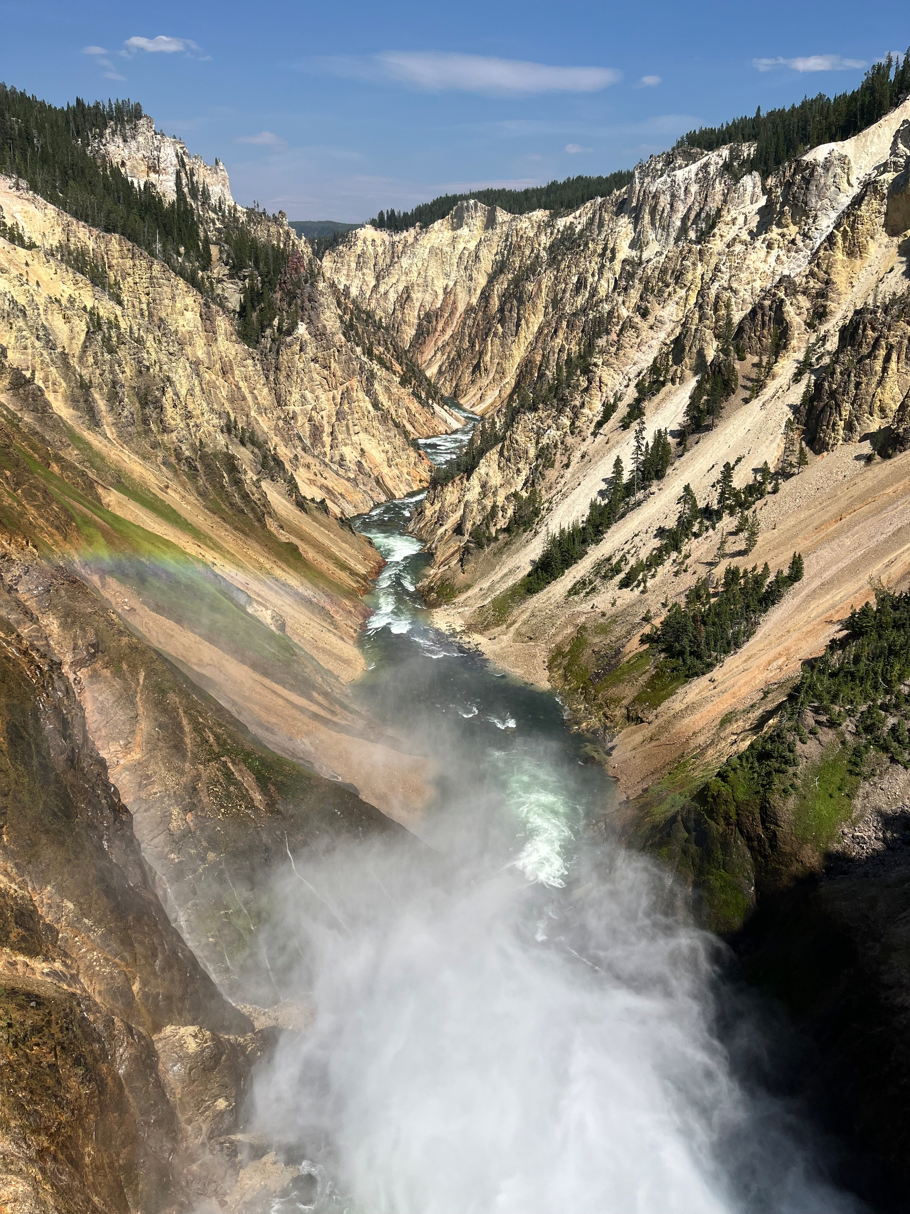 A powerful waterfall cascades into a deep canyon with a river winding through rocky cliffs and a faint rainbow visible in the mist.