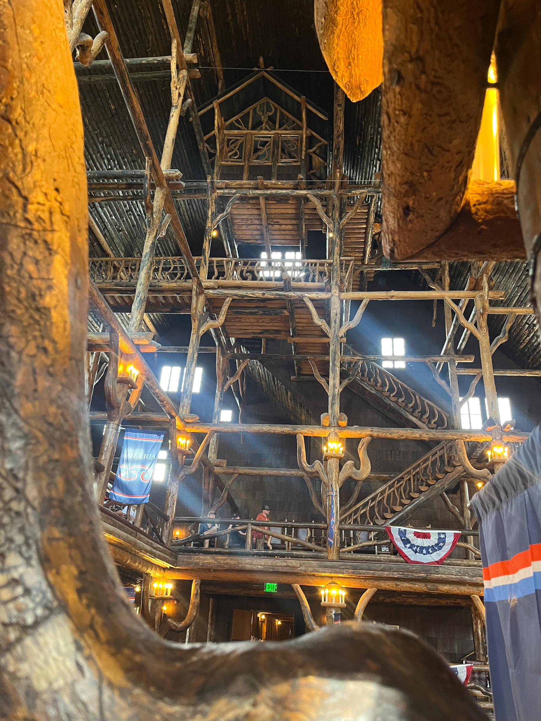 A rustic multi-level wooden lodge interior features large beams, staircases, and windows letting in natural light.