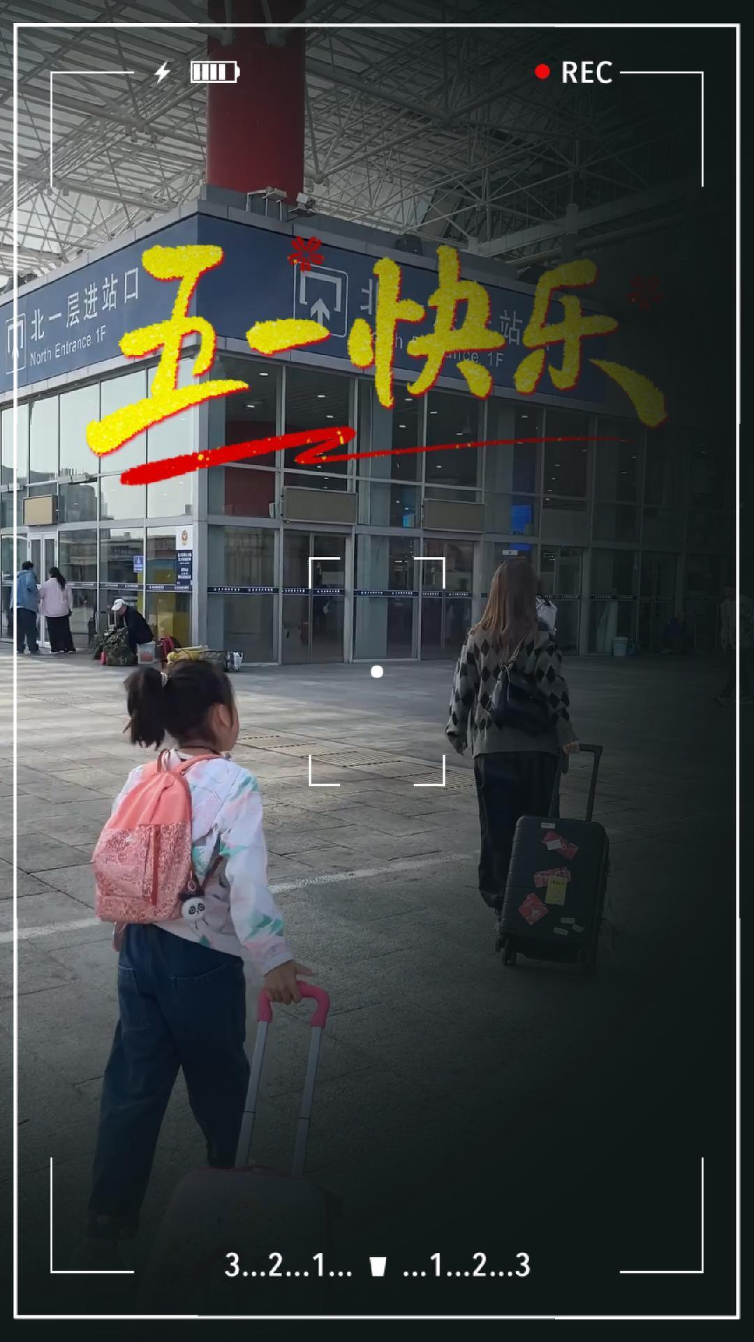 A young girl and an adult are pulling suitcases outside a building, captured in a video frame with colorful text and numerical overlay.