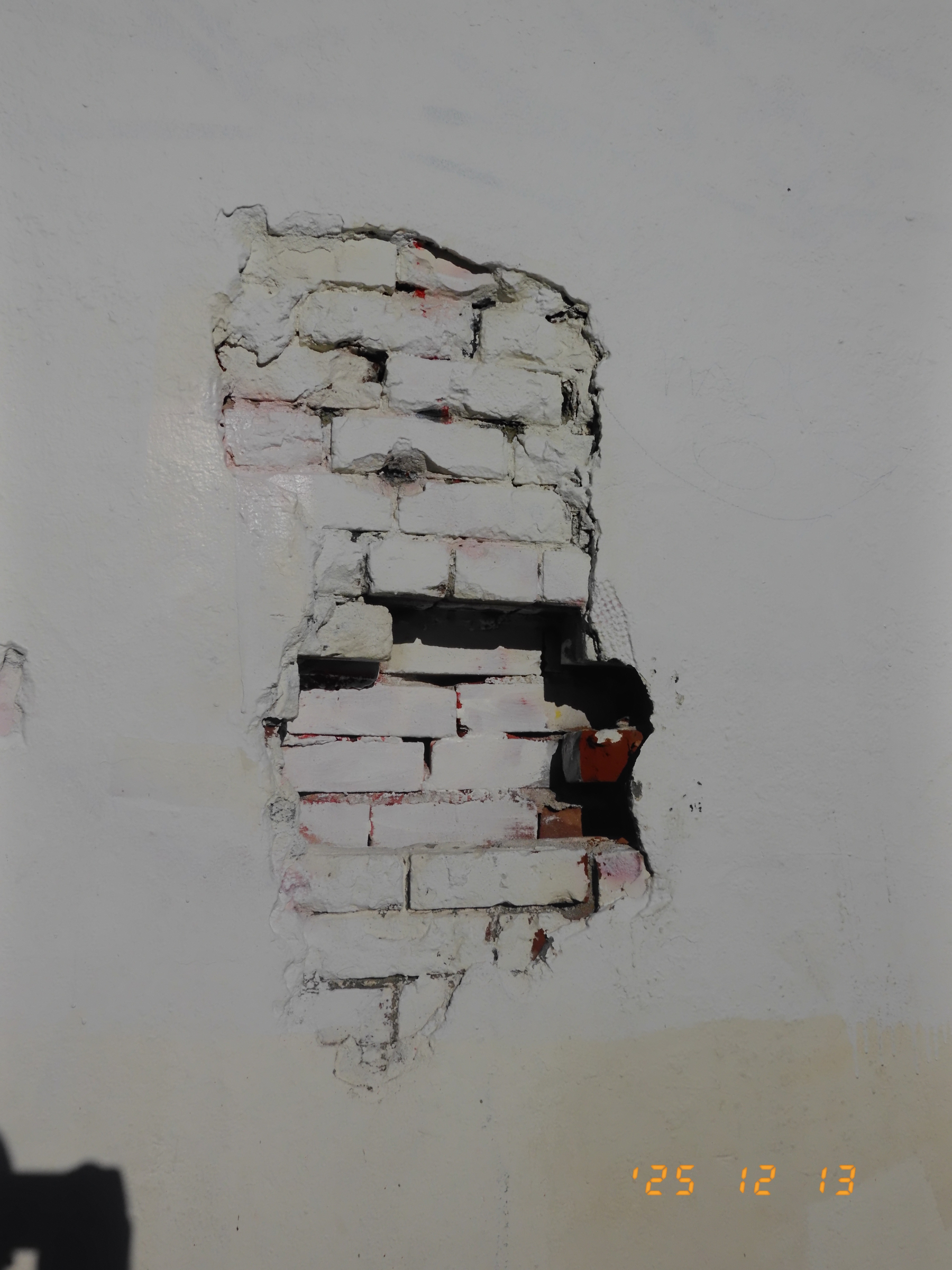 A section of a brick wall is exposed behind peeling and crumbling white plaster.