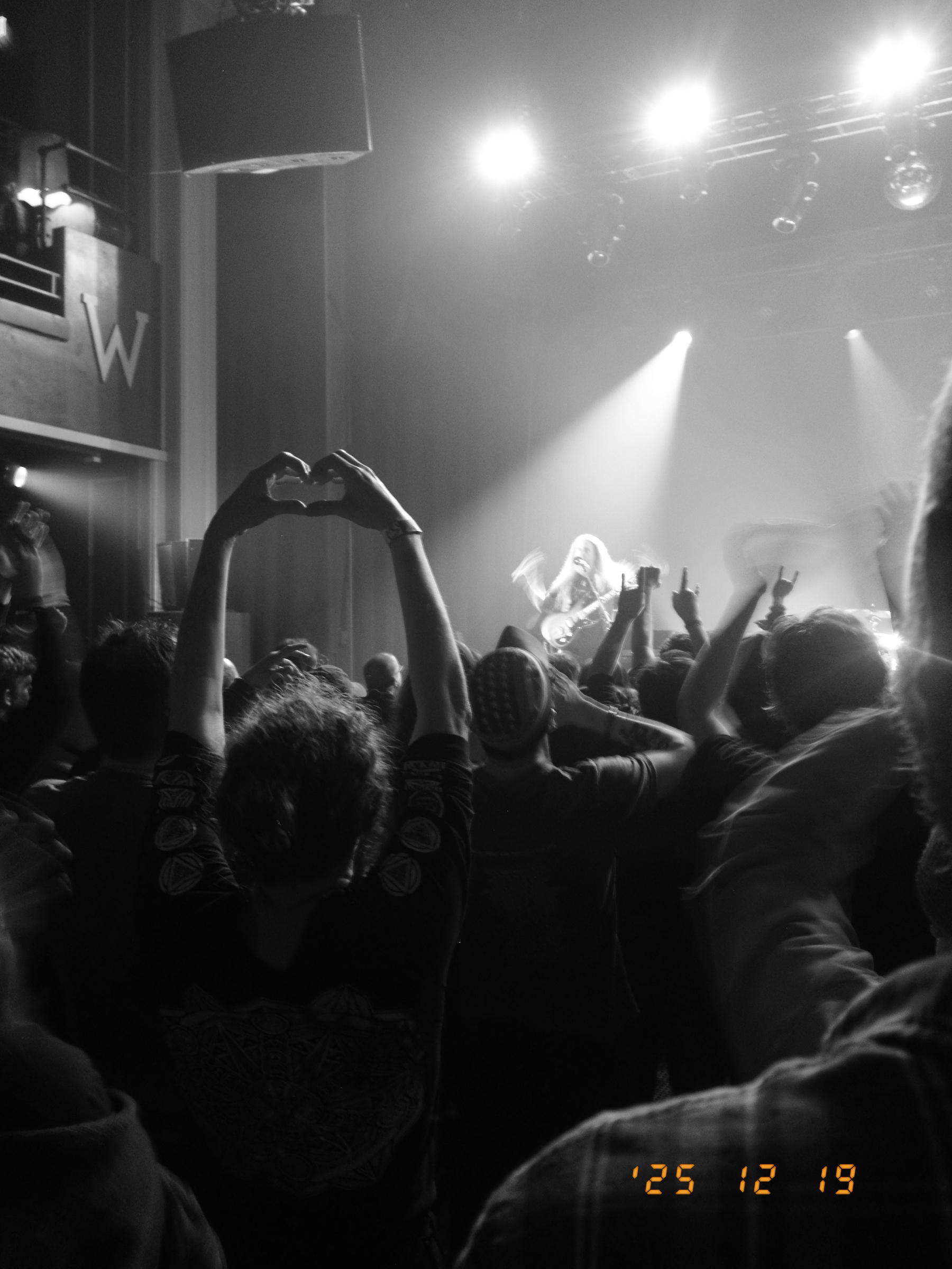 A crowd at a concert is enjoying a performance, with some people raising their hands.