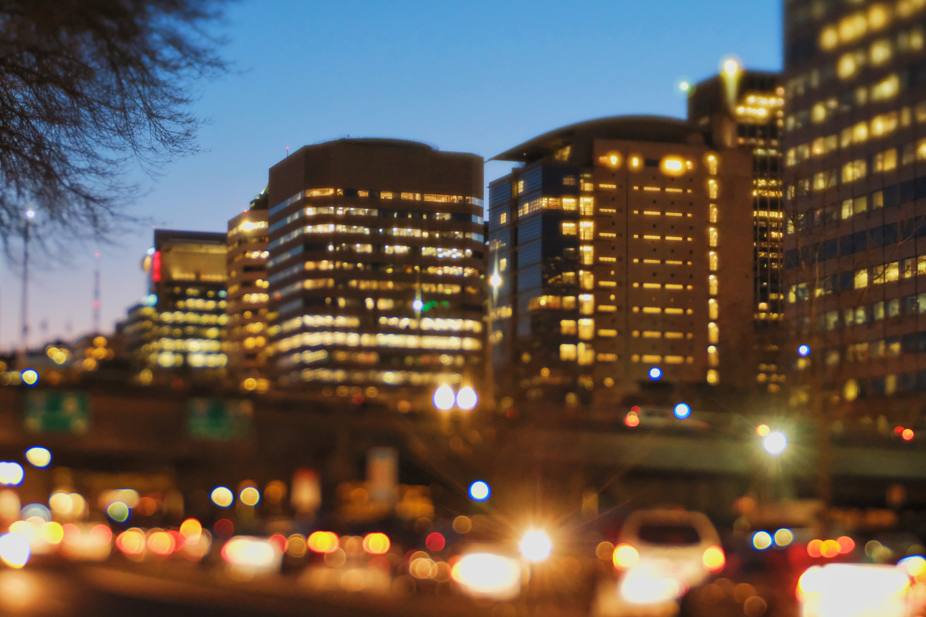 A cityscape at dusk features illuminated skyscrapers and blurred car lights in the foreground, creating a vibrant urban scene.