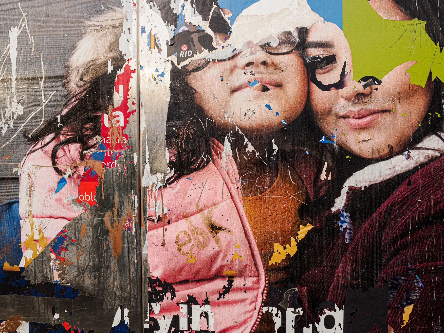 A heavily weathered and torn poster depicts two smiling individuals partly obscured by layers of peeling paper and graffiti.
