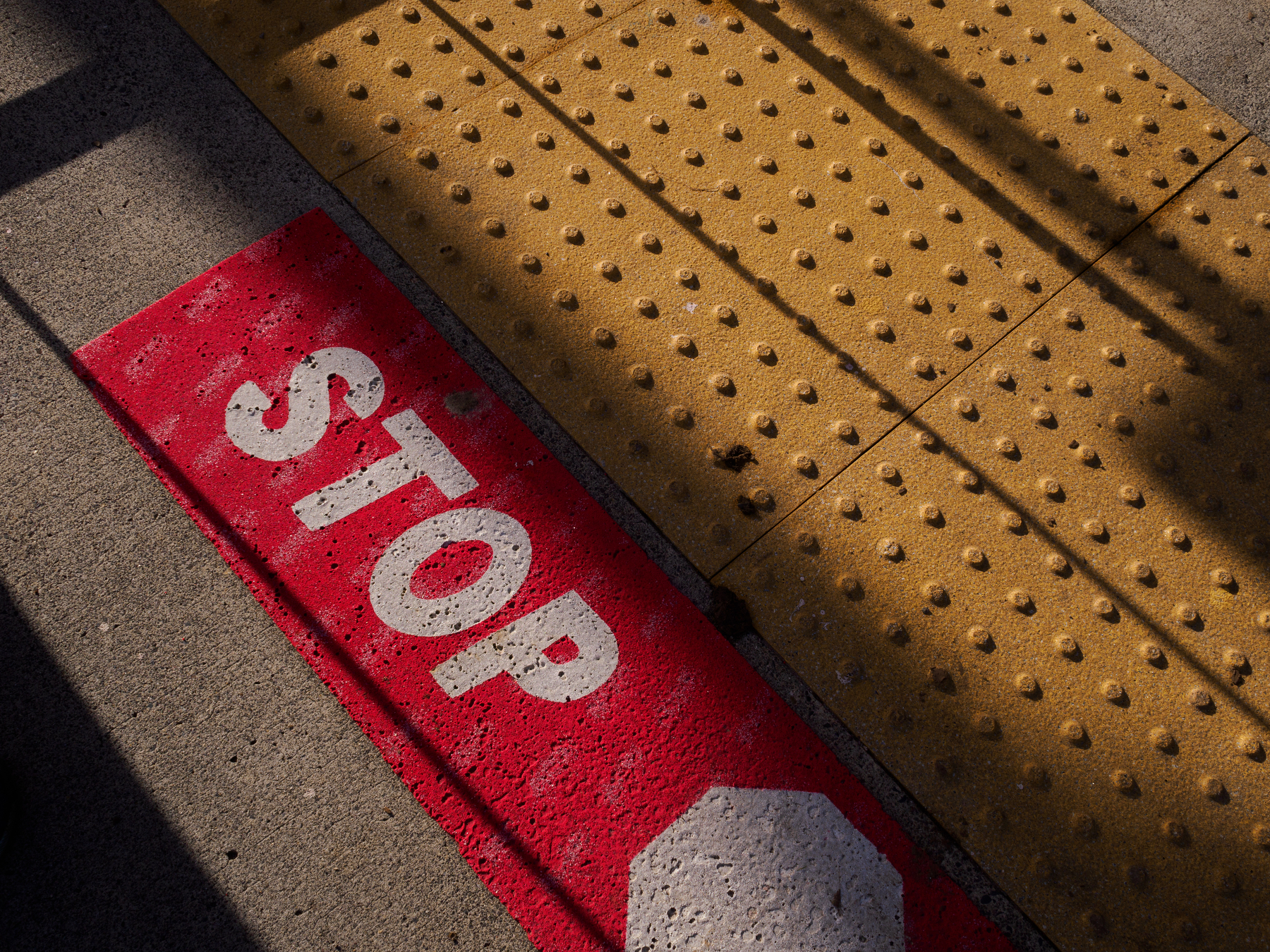 A red pavement marking with the word STOP is adjacent to a textured yellow surface.
