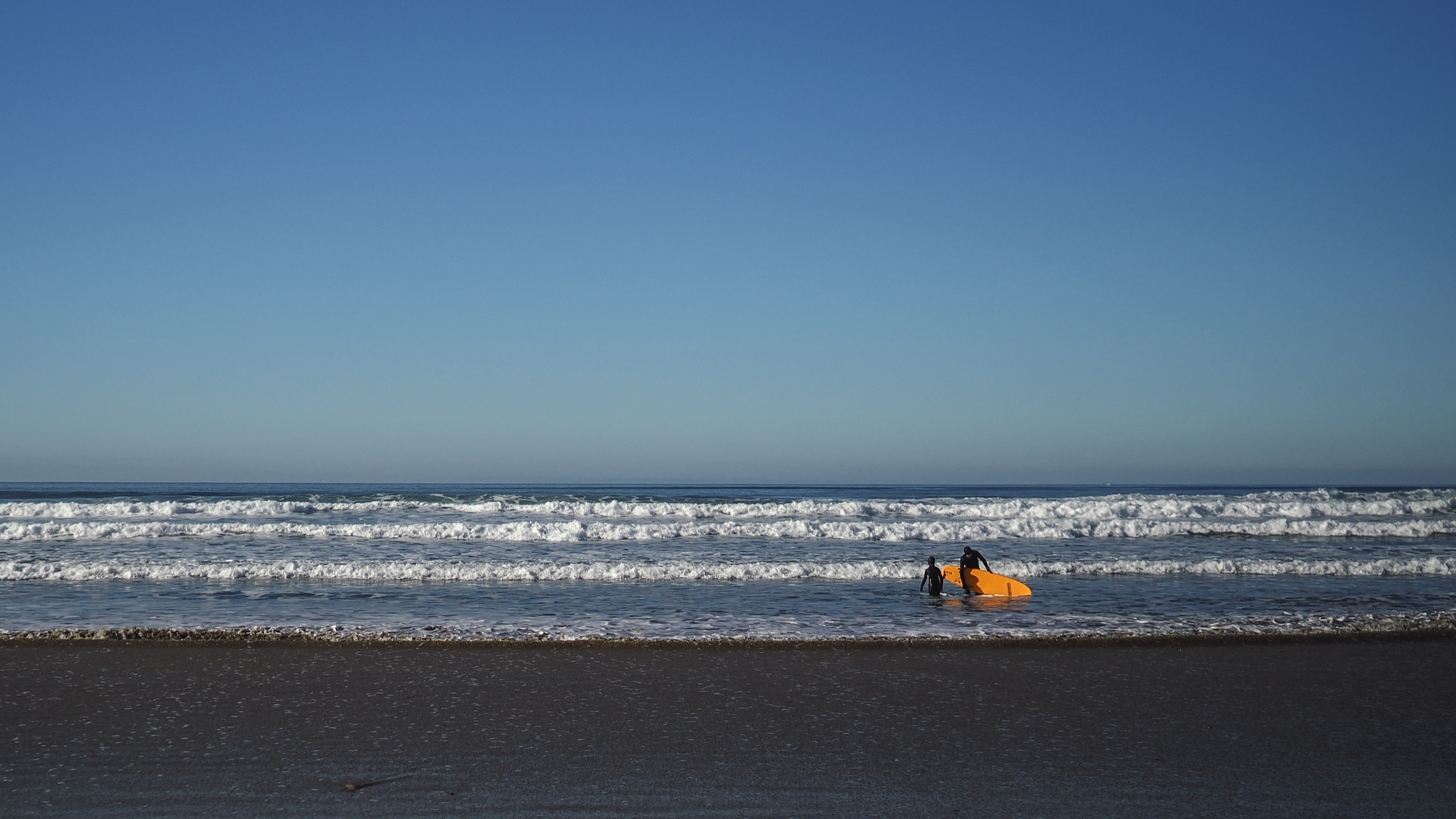 two people  on a sandy beach near the water next to a yellow surfboard