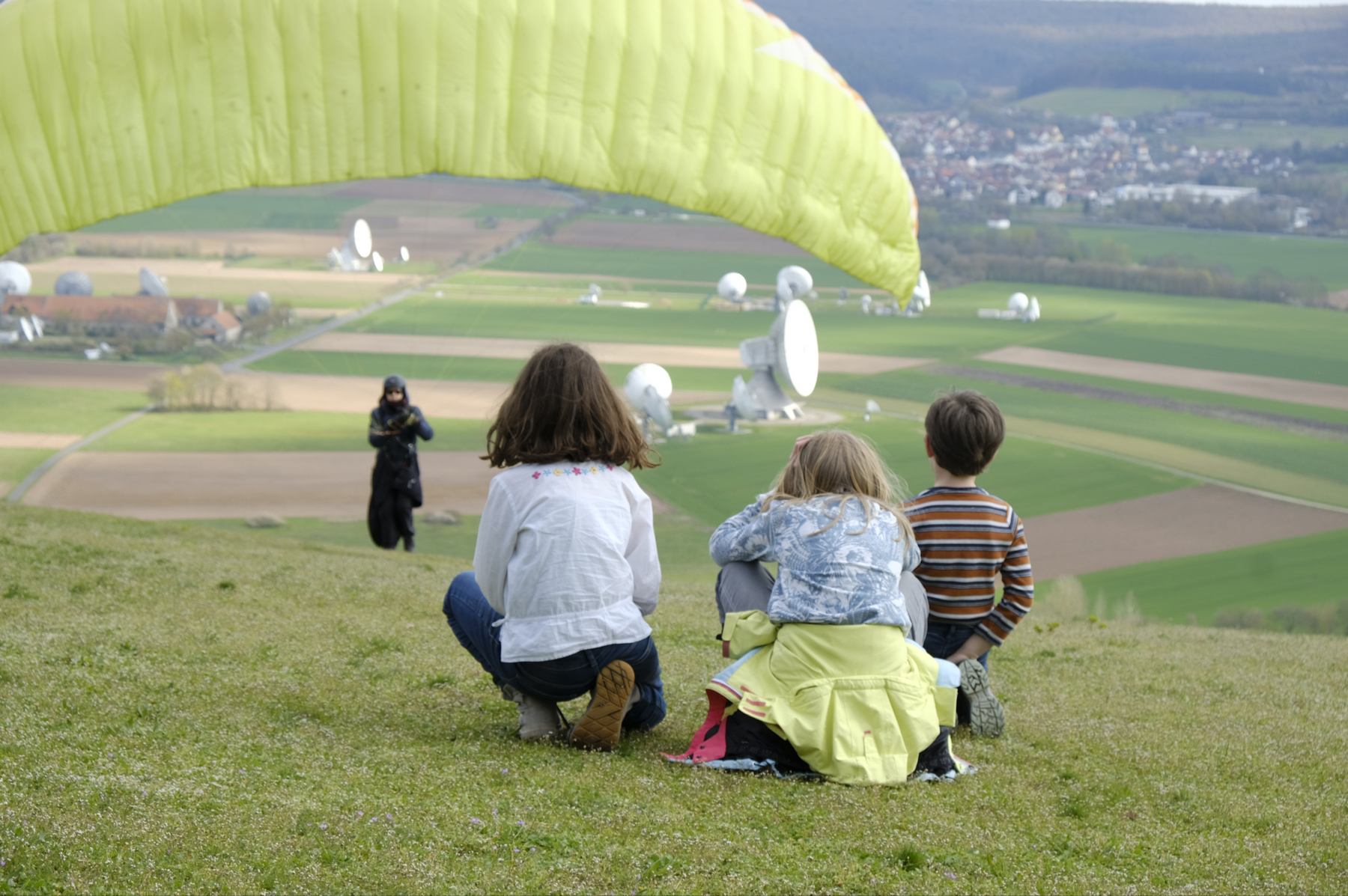 three kids watching a paraglider taking off
