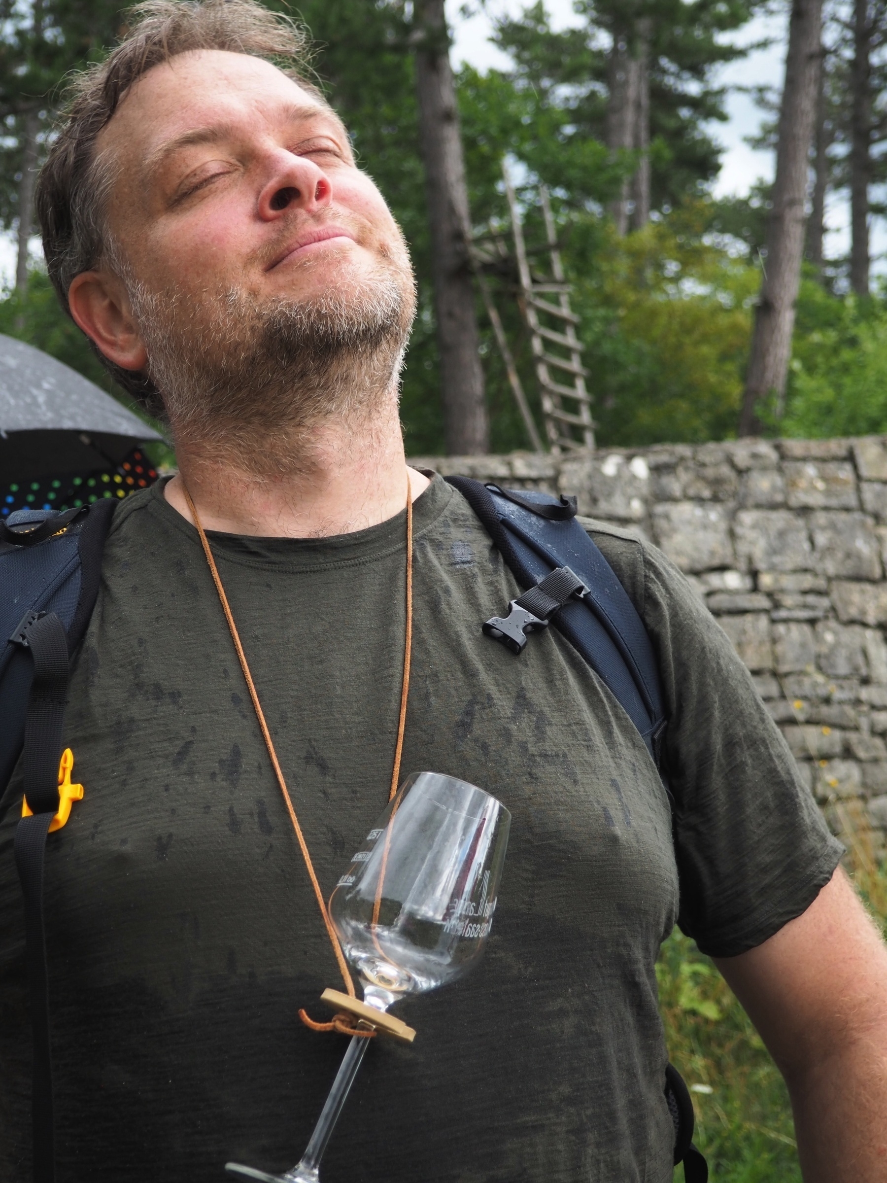 me in with a backpack, closed eyes, face to the skye, enjoying the rain. a wine glass on a rope hanging around my neck