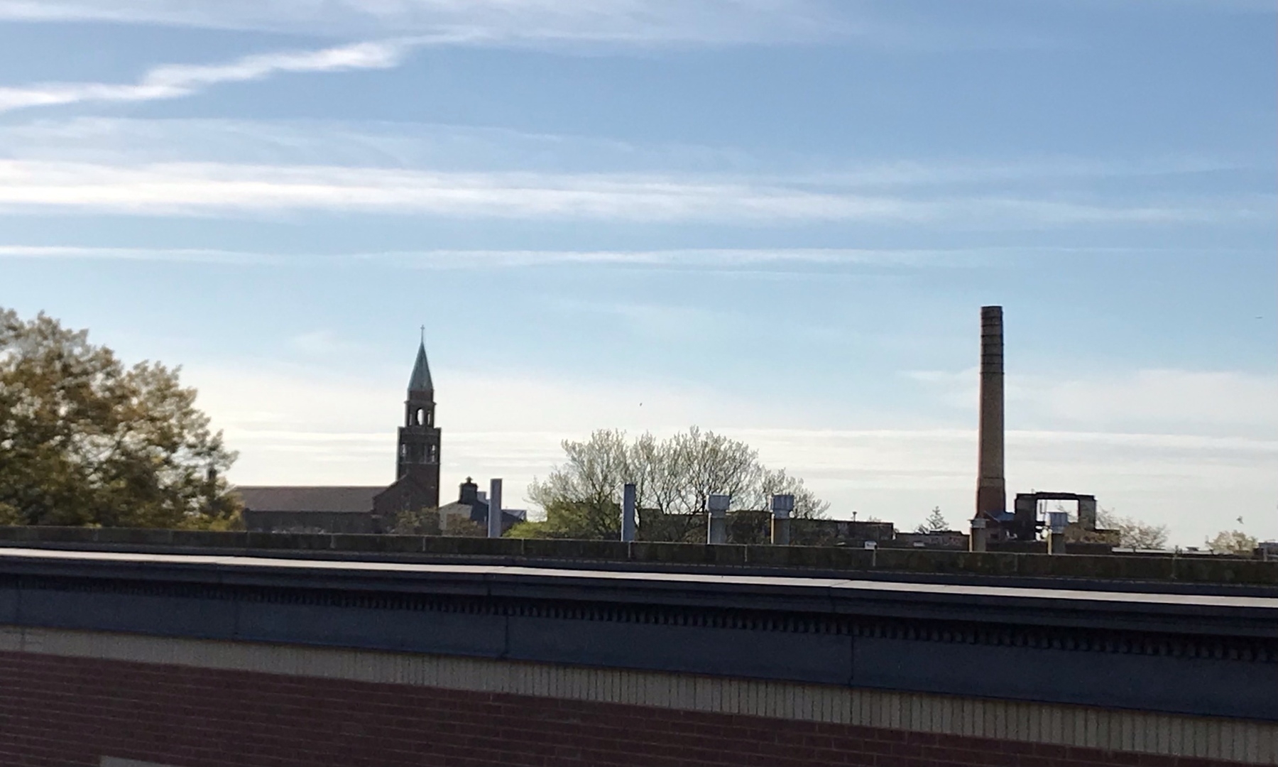 Landscape photo with church steeple and smokestack standing out against the horizon, viewed across the top of a building