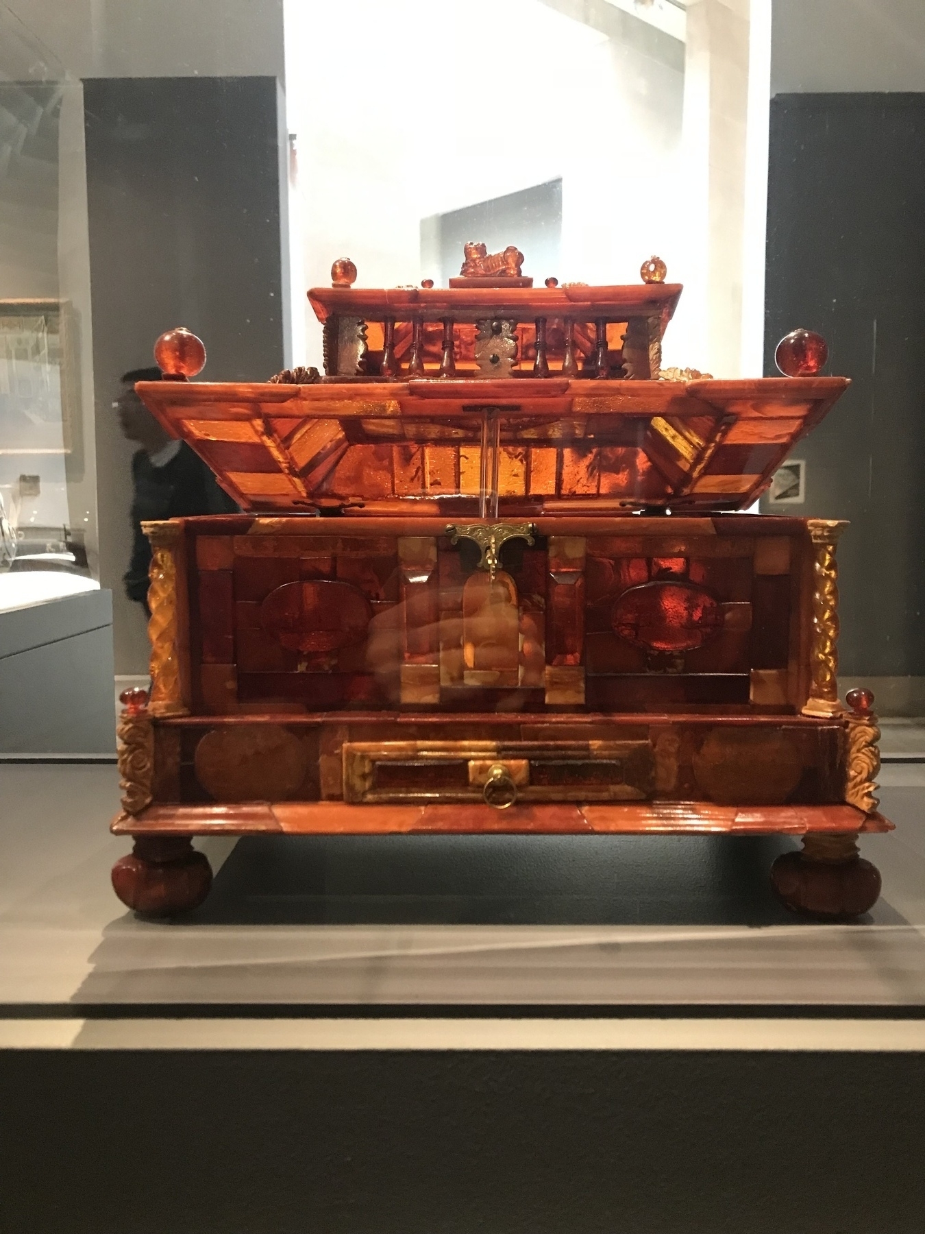 Small ornate chest in a museum, with lid propped open, made of panels of amber with light coming through