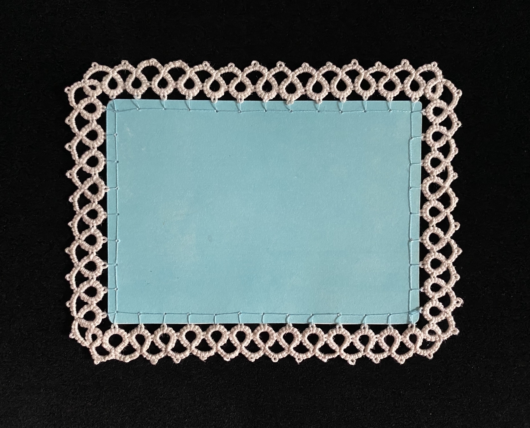 Aqua-colored postcard with a cream tatted lace edging around it (back)