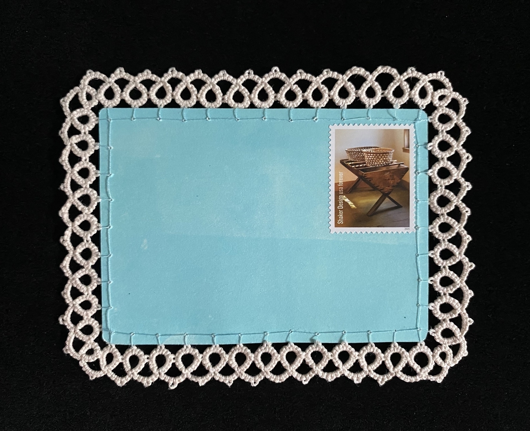 Aqua-colored postcard with a stamp and a cream tatted lace edging around it (front)