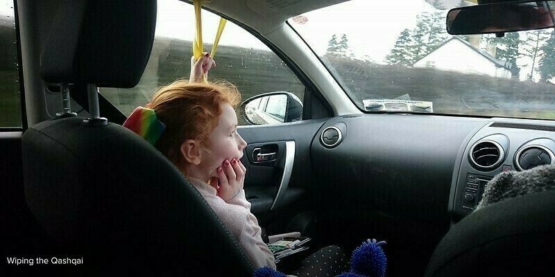 Mia sitting in a the Qashqai, looking out the window while holding yellow straps connected to the windscreen wipers.