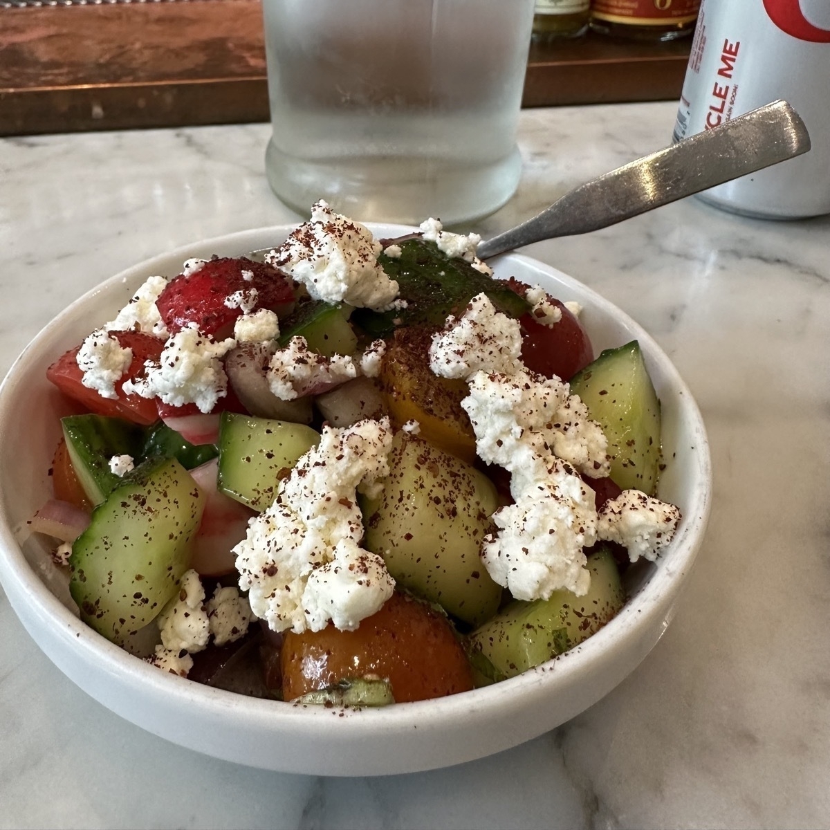 A Greek chopped salad in a small white bowel on a marble-like surface.