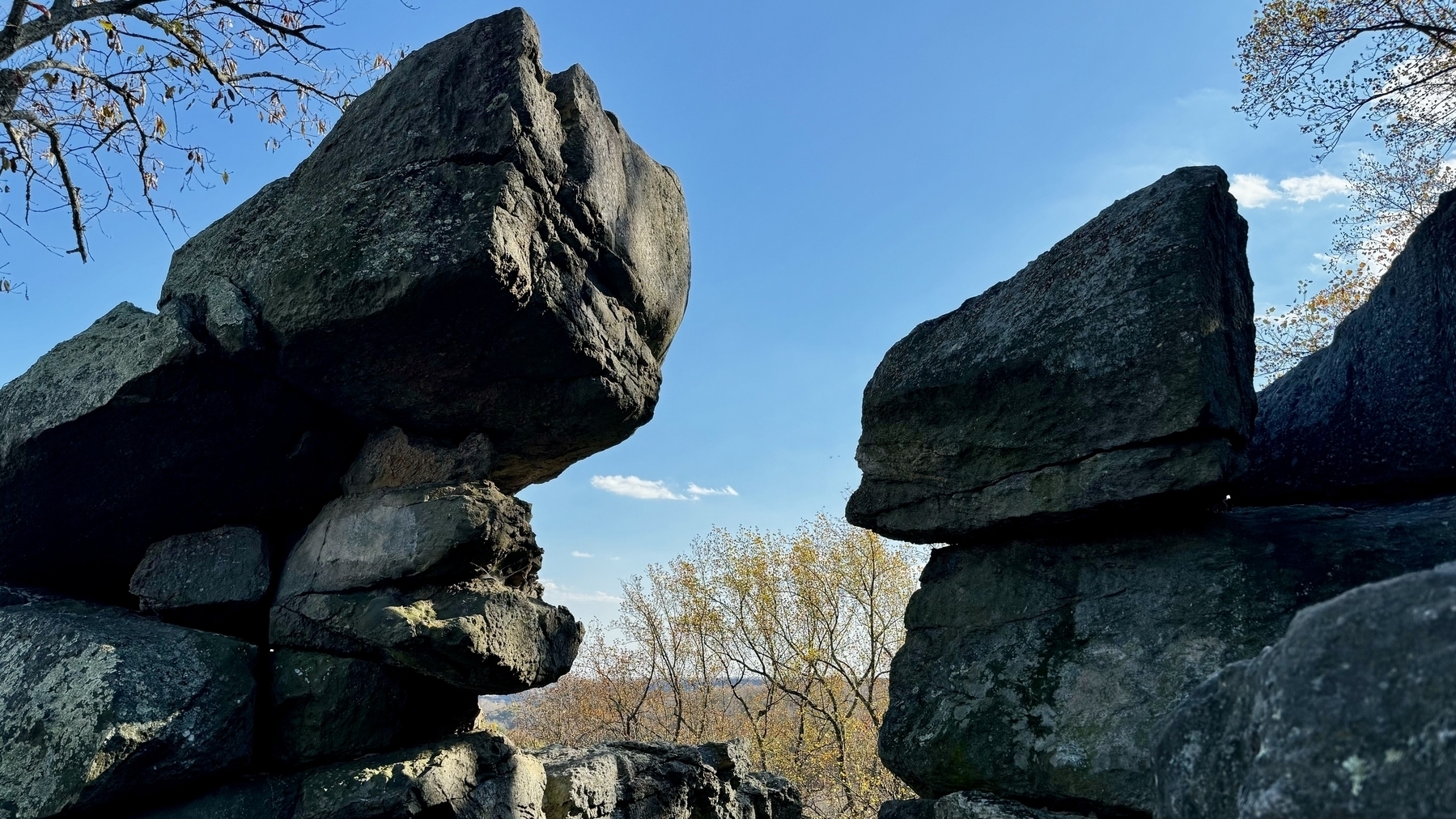 Two large columns of prism-like stone boulders framing a clear sky and tree tops