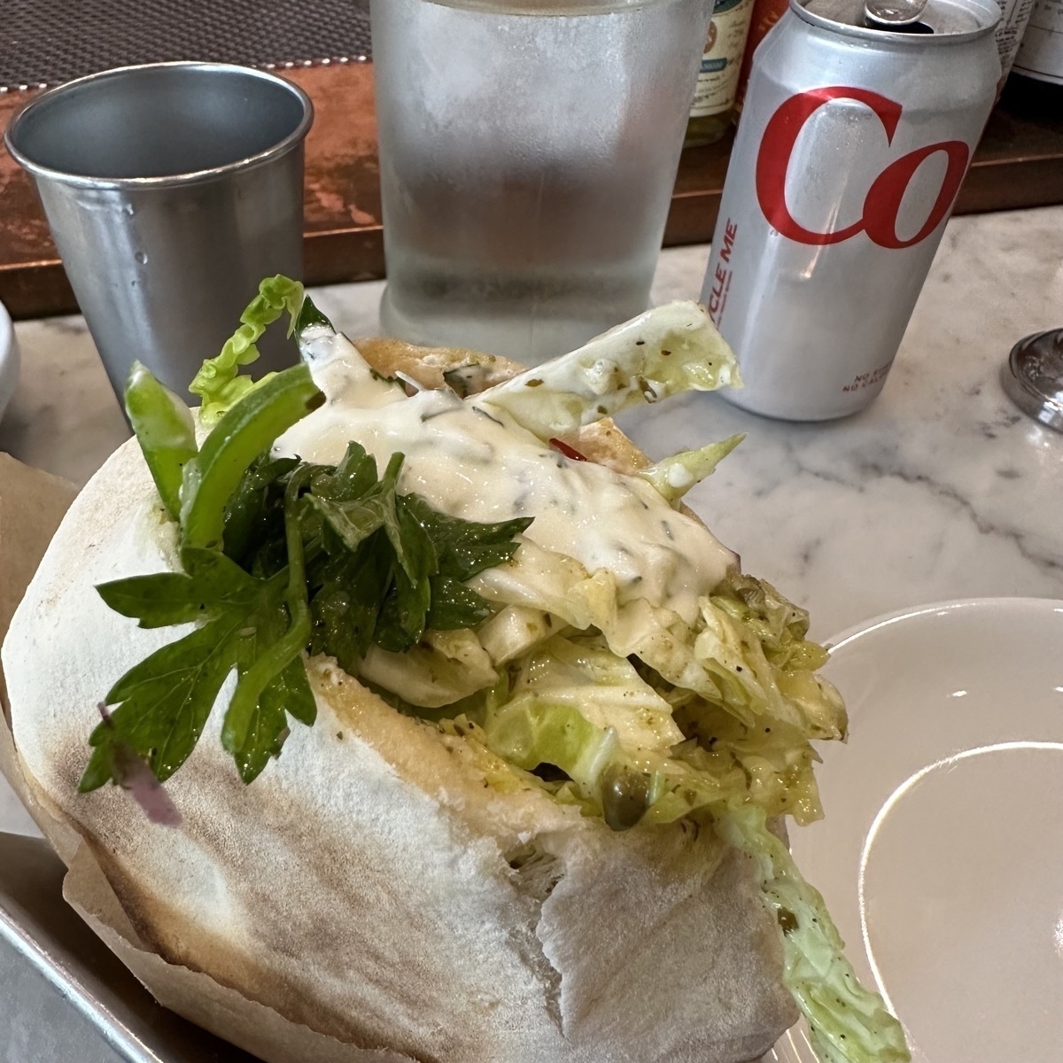 A lamb gyro in a pita held in a metal rack for pitas or tacos on a marble-like surface.