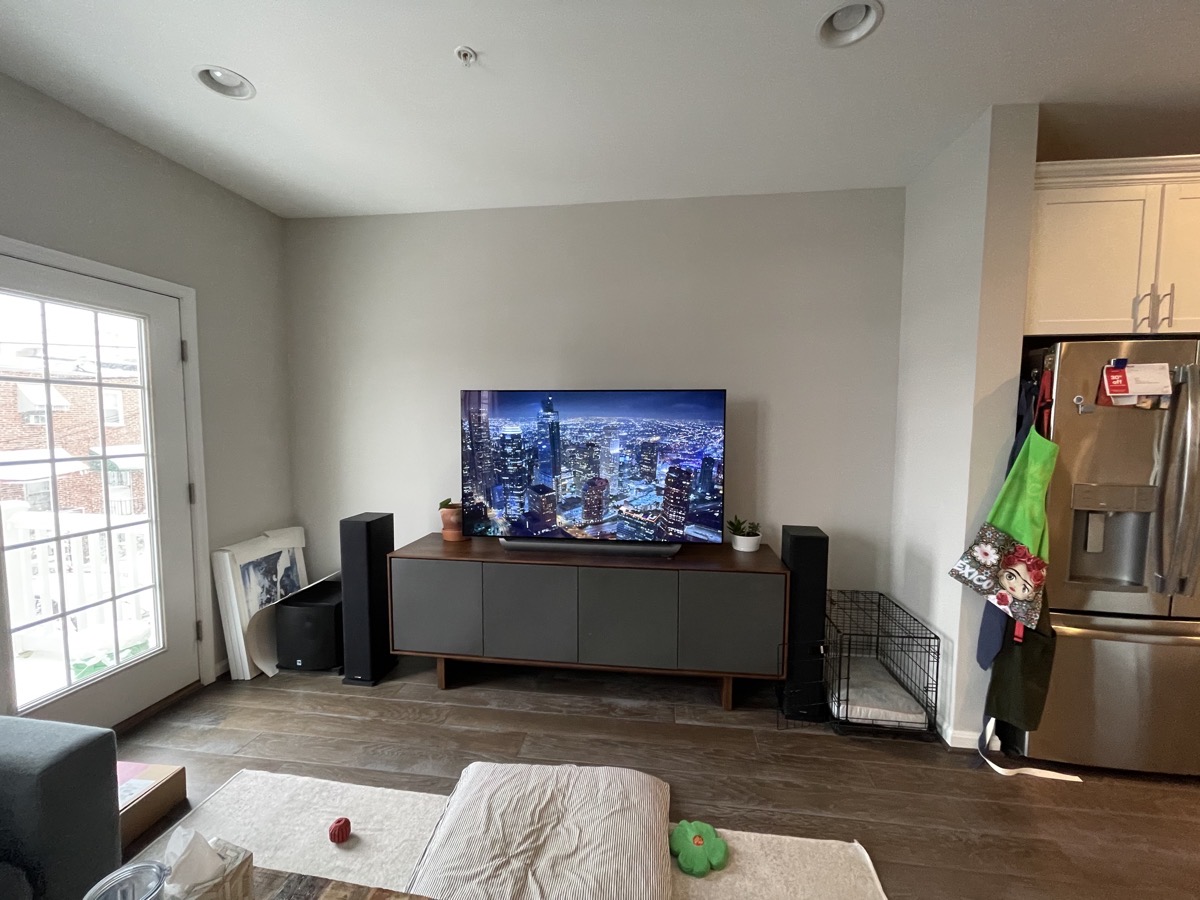 A living room with a TV on a walnut stand with gray doors and two black floor standing speakers.