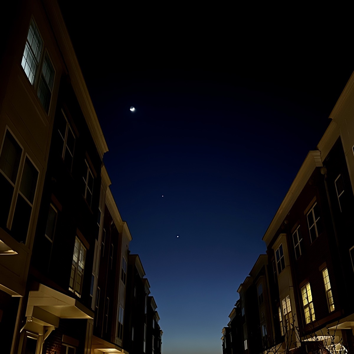 The moon aligned diagonally with Venus and Jupiter between brick townhomes.