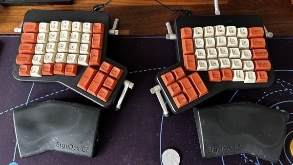 Ergodox EZ keyboard with orange and beige keycaps on a purple desk mat.