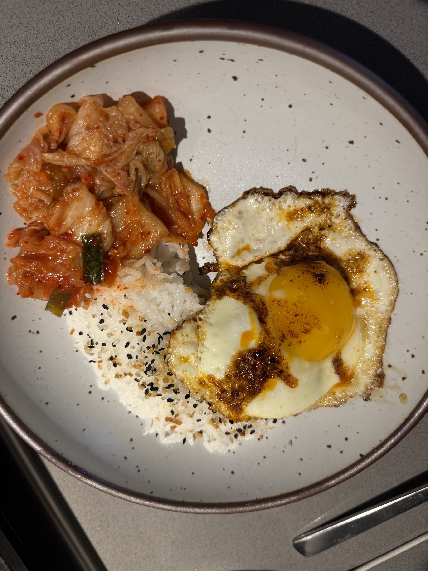 A plate features fried egg, seasoned rice with sesame seeds, and a serving of kimchi.