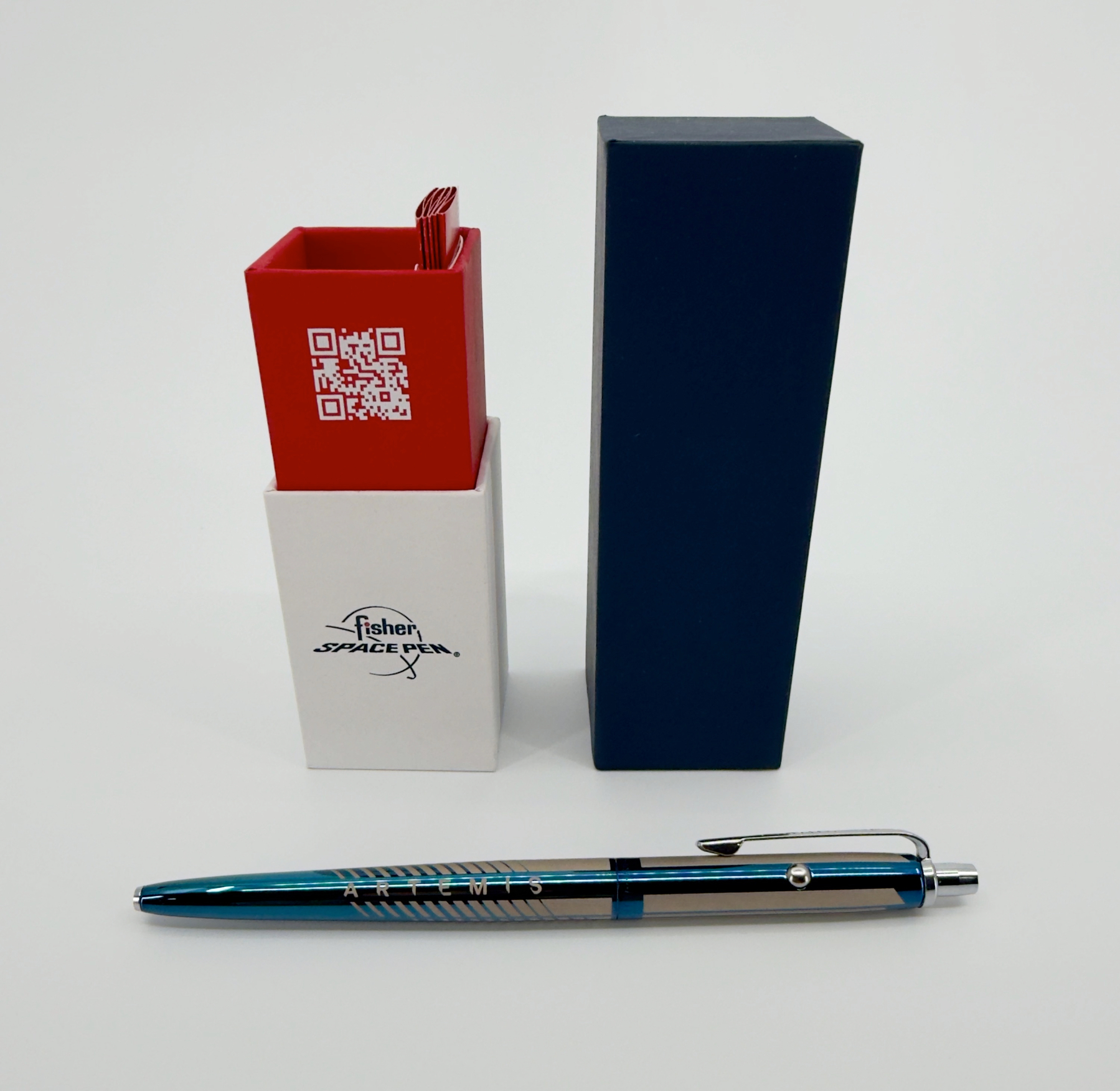 Auto-generated description: A Fisher Space Pen is displayed with its packaging, featuring a blue box, a white holder with the logo, and a red section with a QR code.