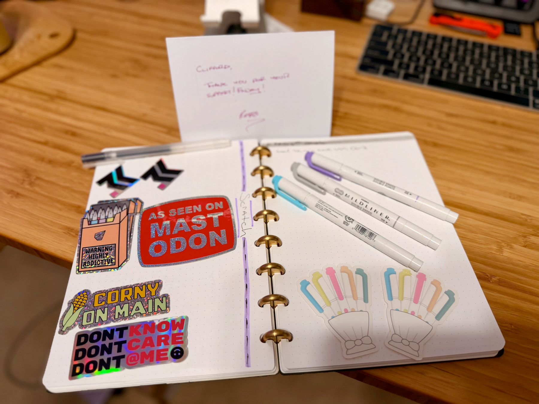 Auto-generated description: An open planner decorated with colorful stickers and surrounded by markers on a wooden table.