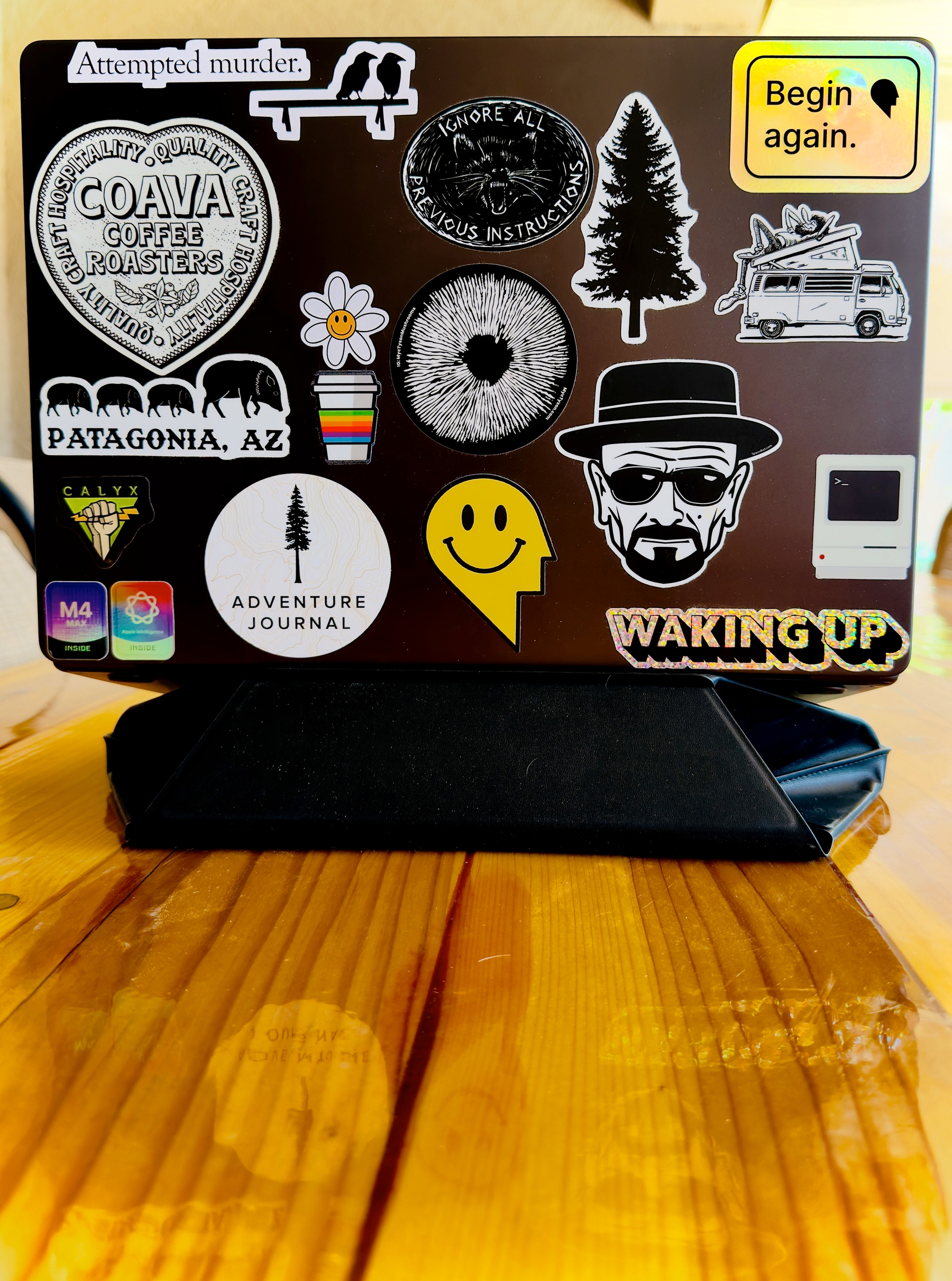 Auto-generated description: A laptop cover is adorned with various stickers, including a smiley face, tree designs, and quirky phrases like Attempted murder.
